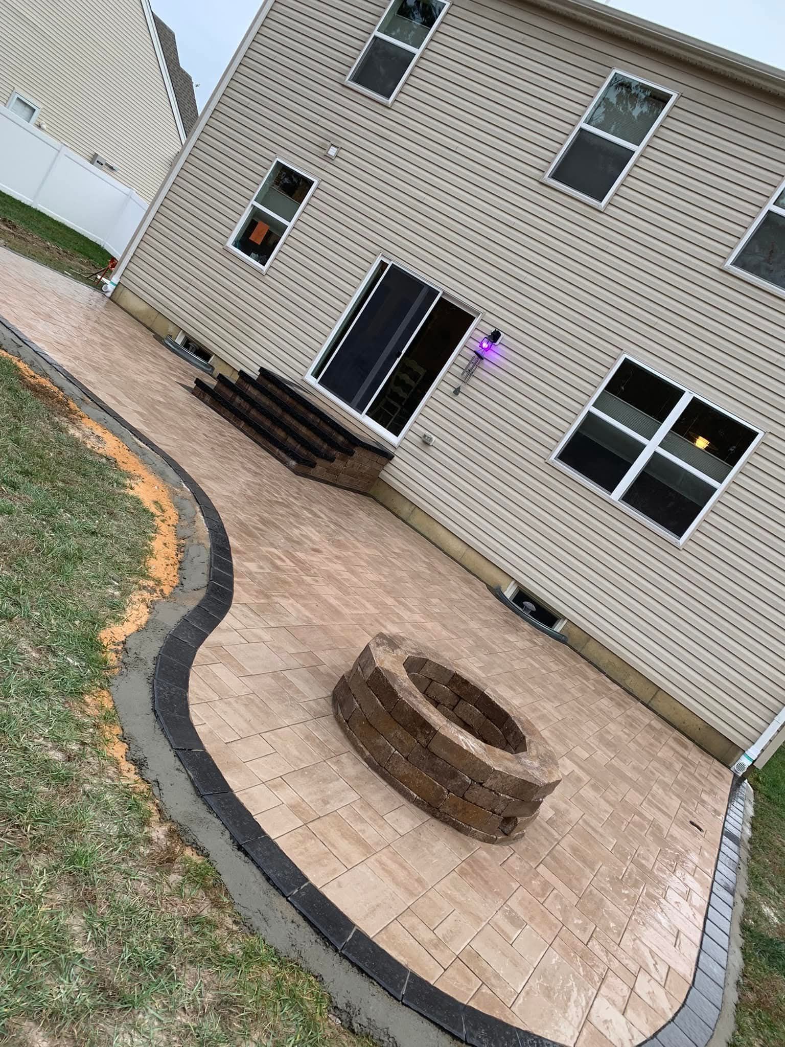 Backyard patio with stone pavers, fire pit, and house with multiple windows.
