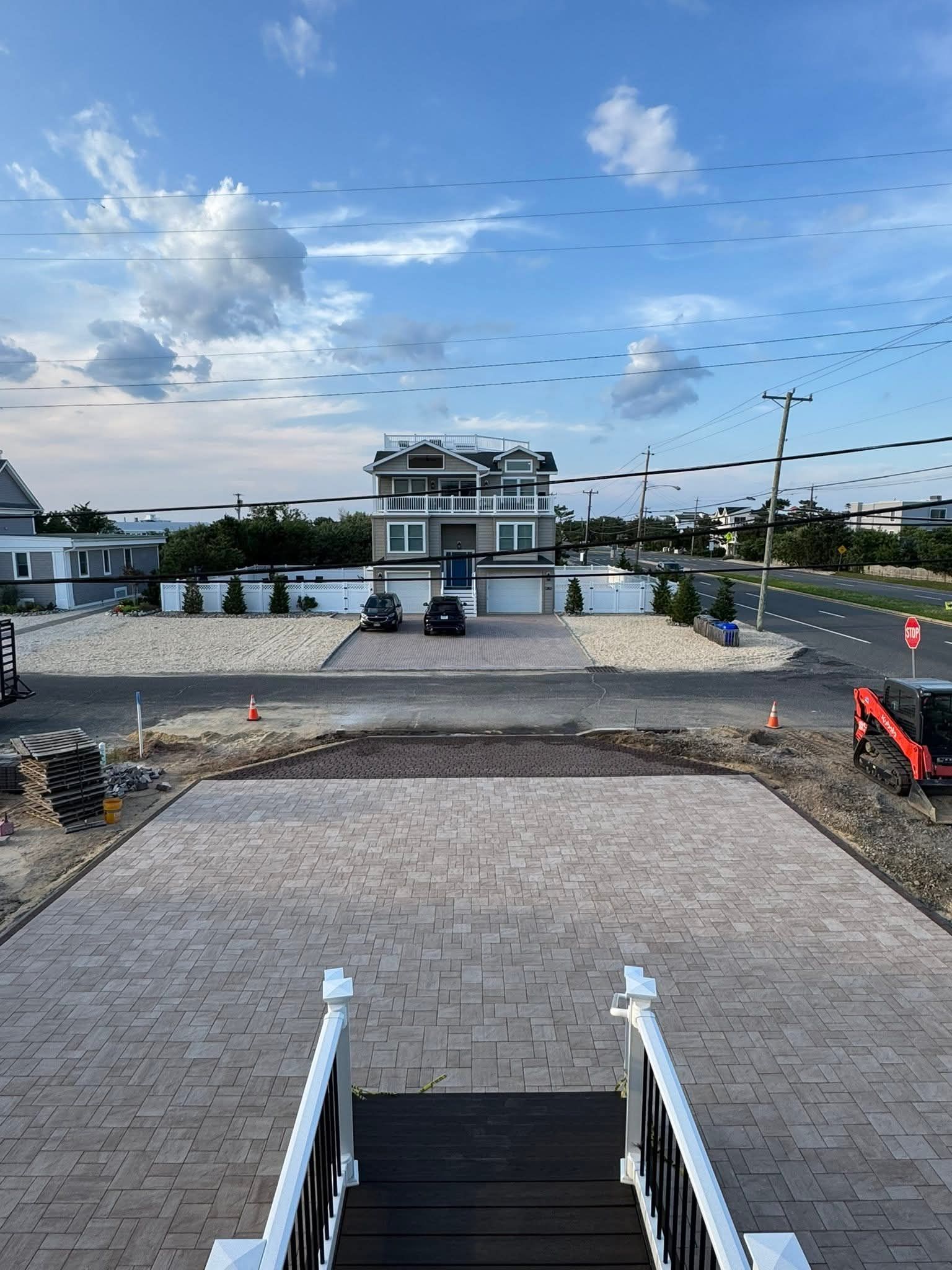 A multi-story modern beach house with a paved drive and blue sky.