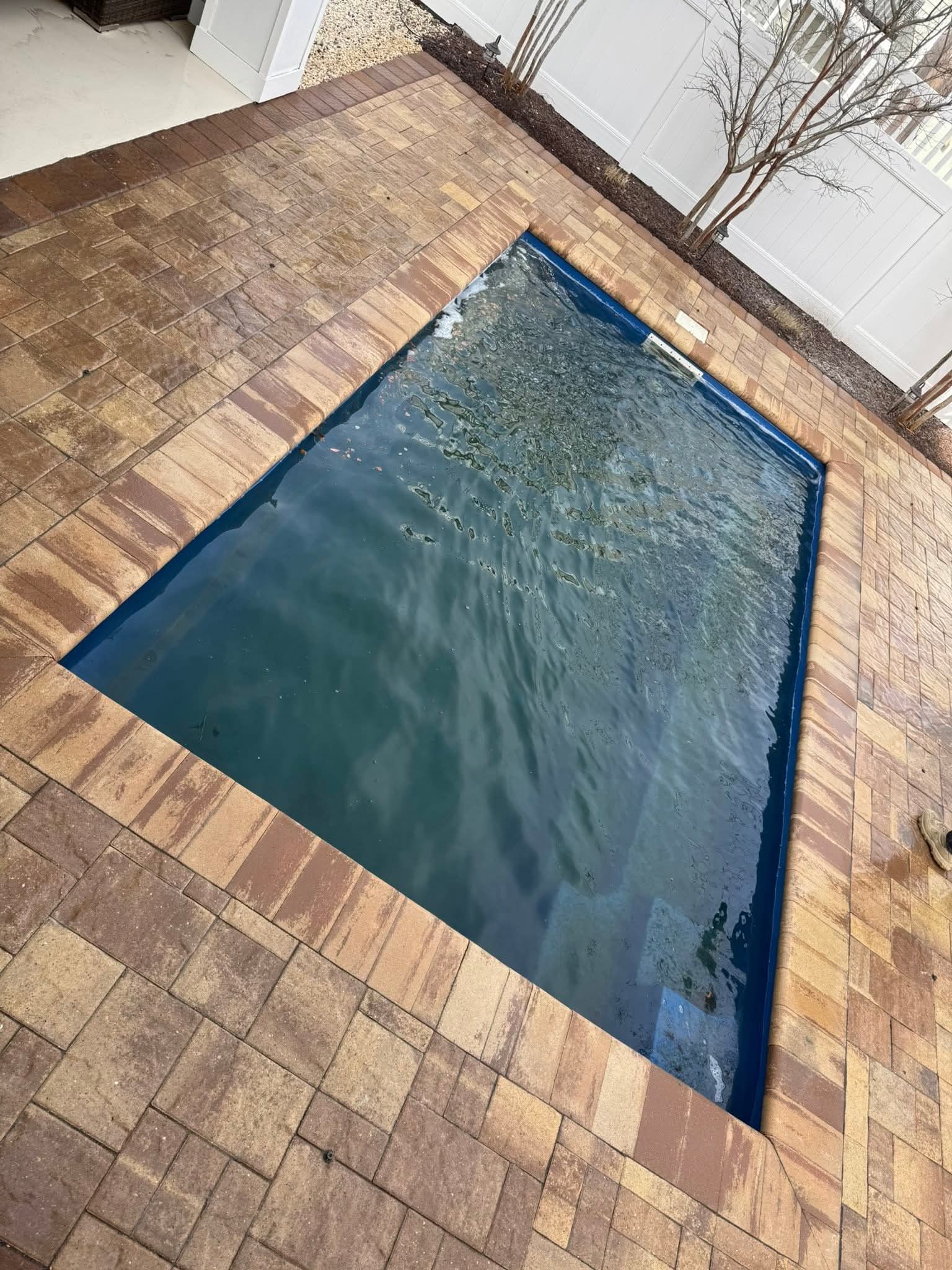 A rectangular pool with water surrounded by brick pavers.