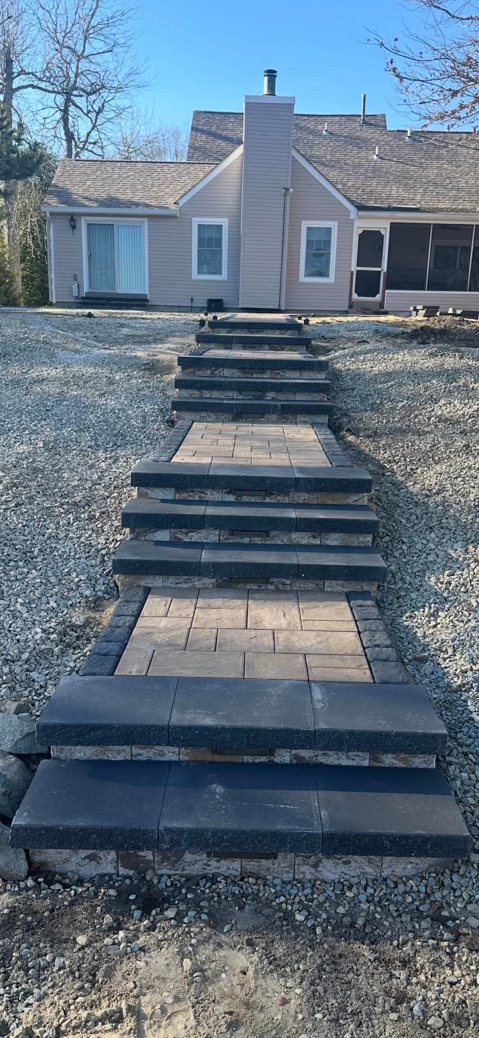 Stone steps leading up to a light-colored house with chimney, set on a gravel path under a blue sky.