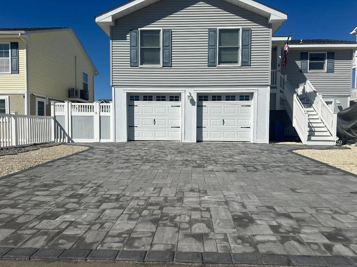 Driveway paved with gray bricks in front of a two-car garage, blue house, blue shutters.