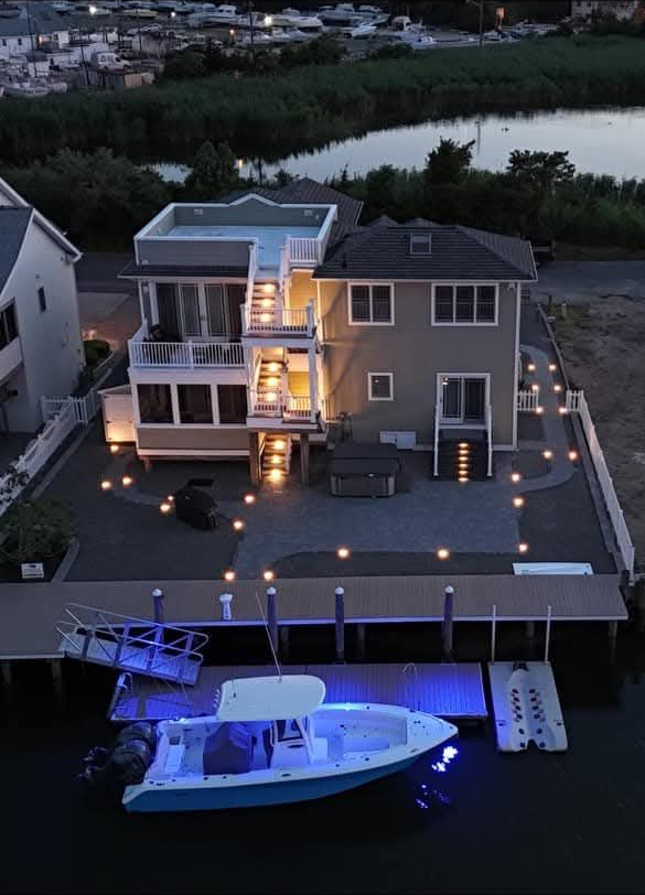 A two-story house at dusk with boat dock and lit boat on water.