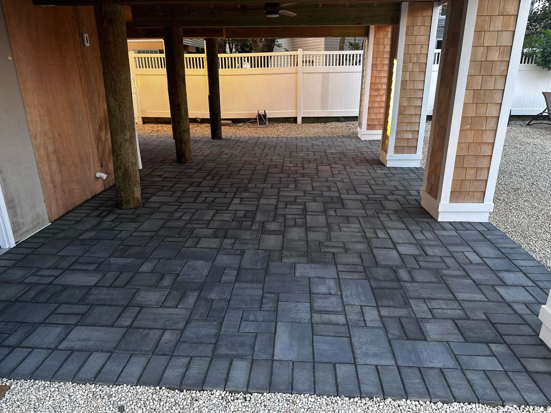 Brick patio under a raised building with wooden support beams and white fence.
