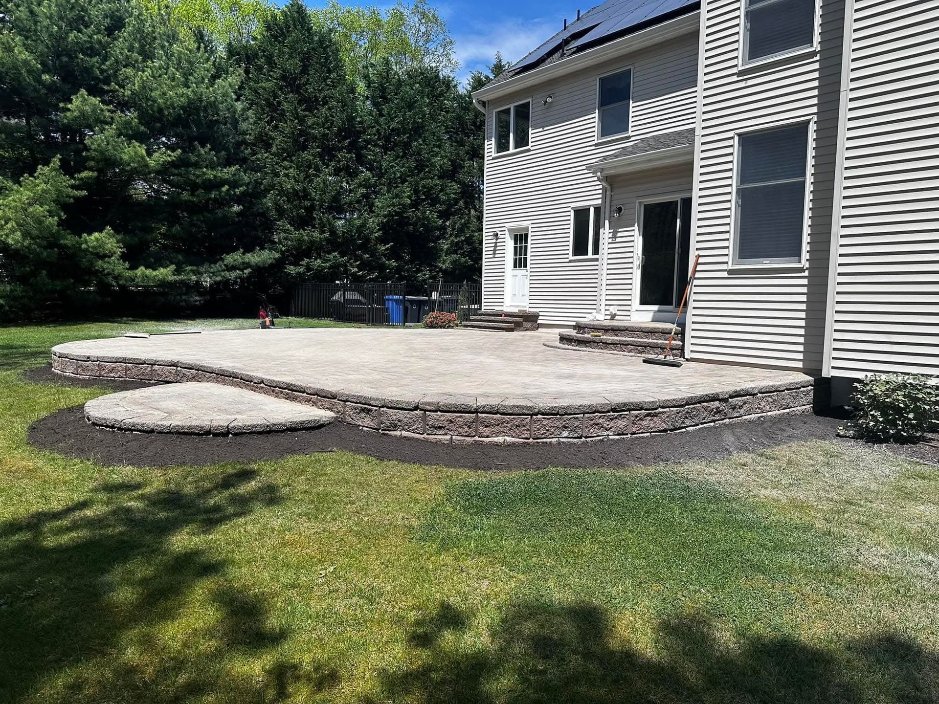 Stone patio with retaining wall in a backyard next to a two-story house.