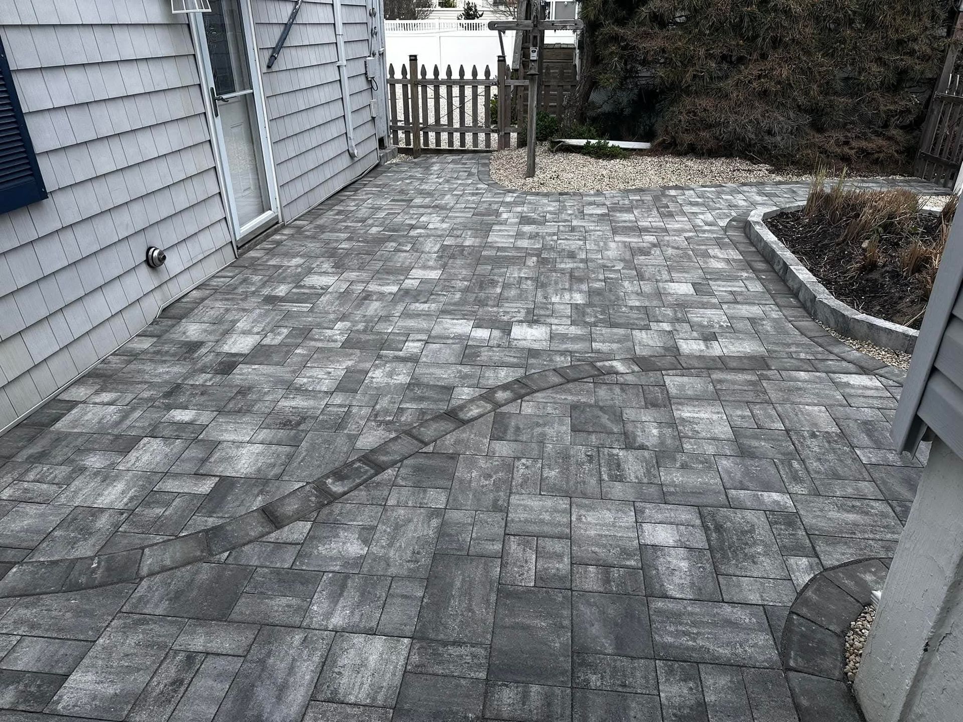 Brick patio outside a house with a dark gray, curved design and a small wooden gate.