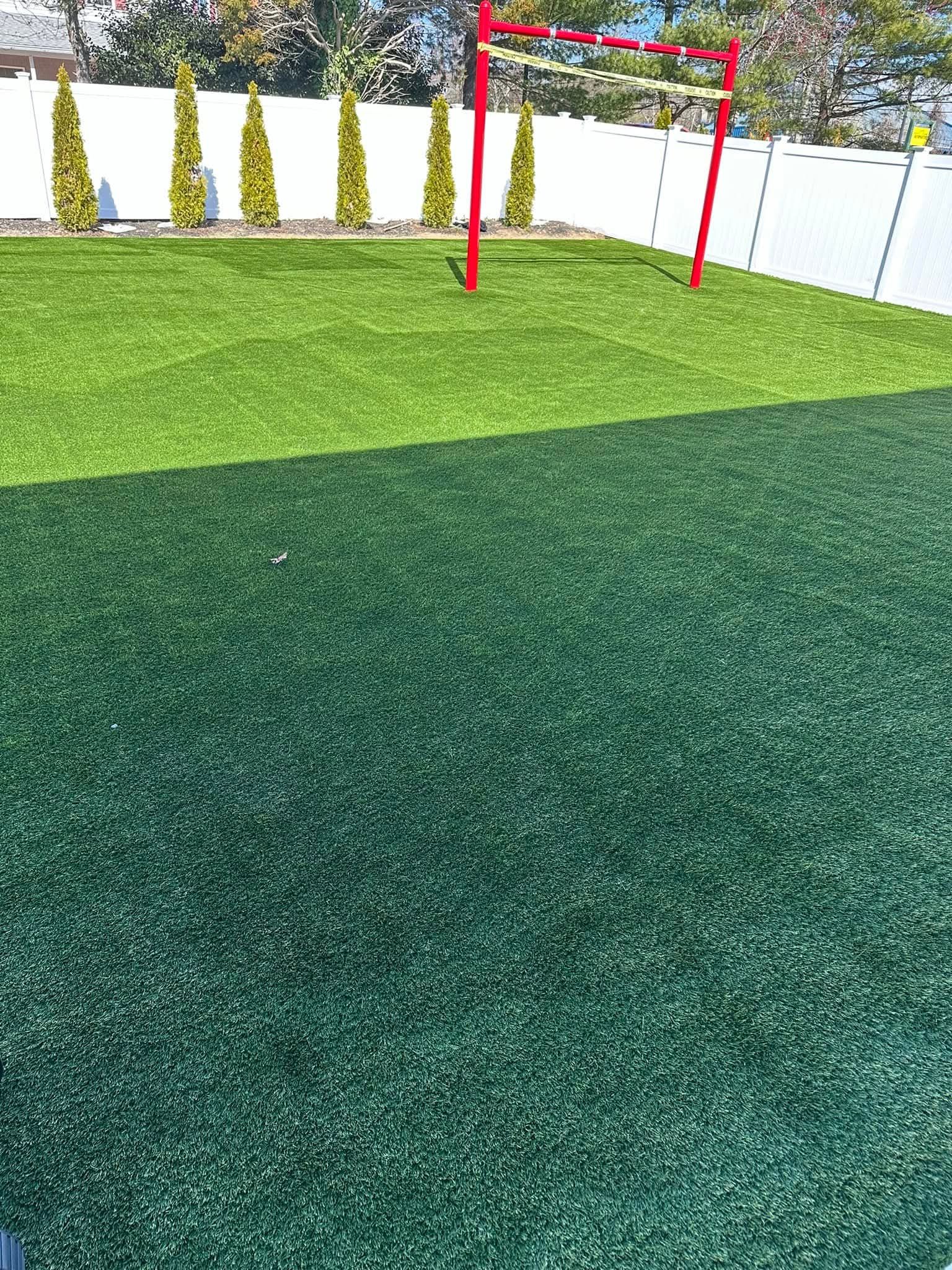 Green artificial turf yard with red ladder game, white fence, and trees.