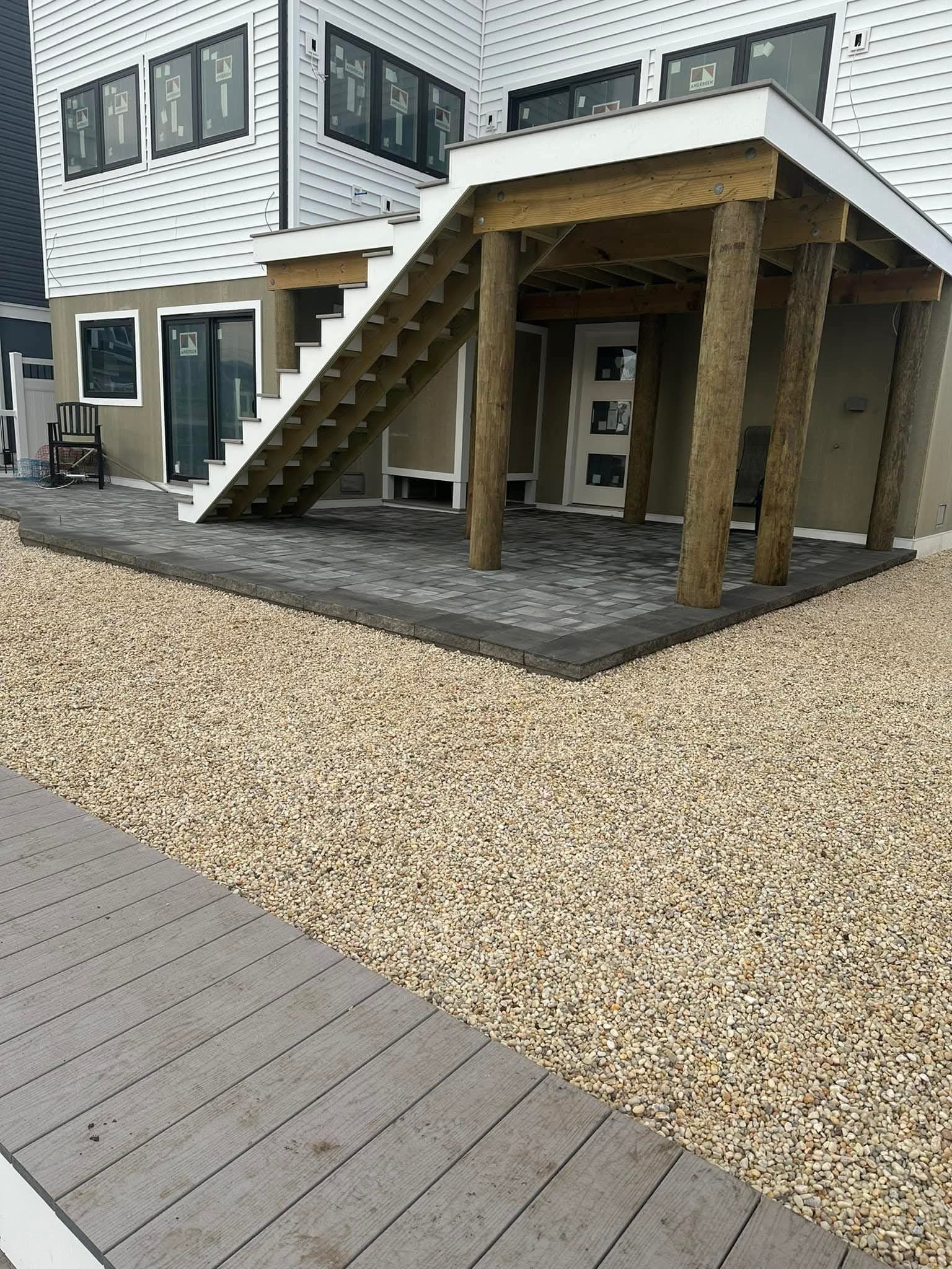 A house with a wooden staircase, stone patio, and gravel landscaping.