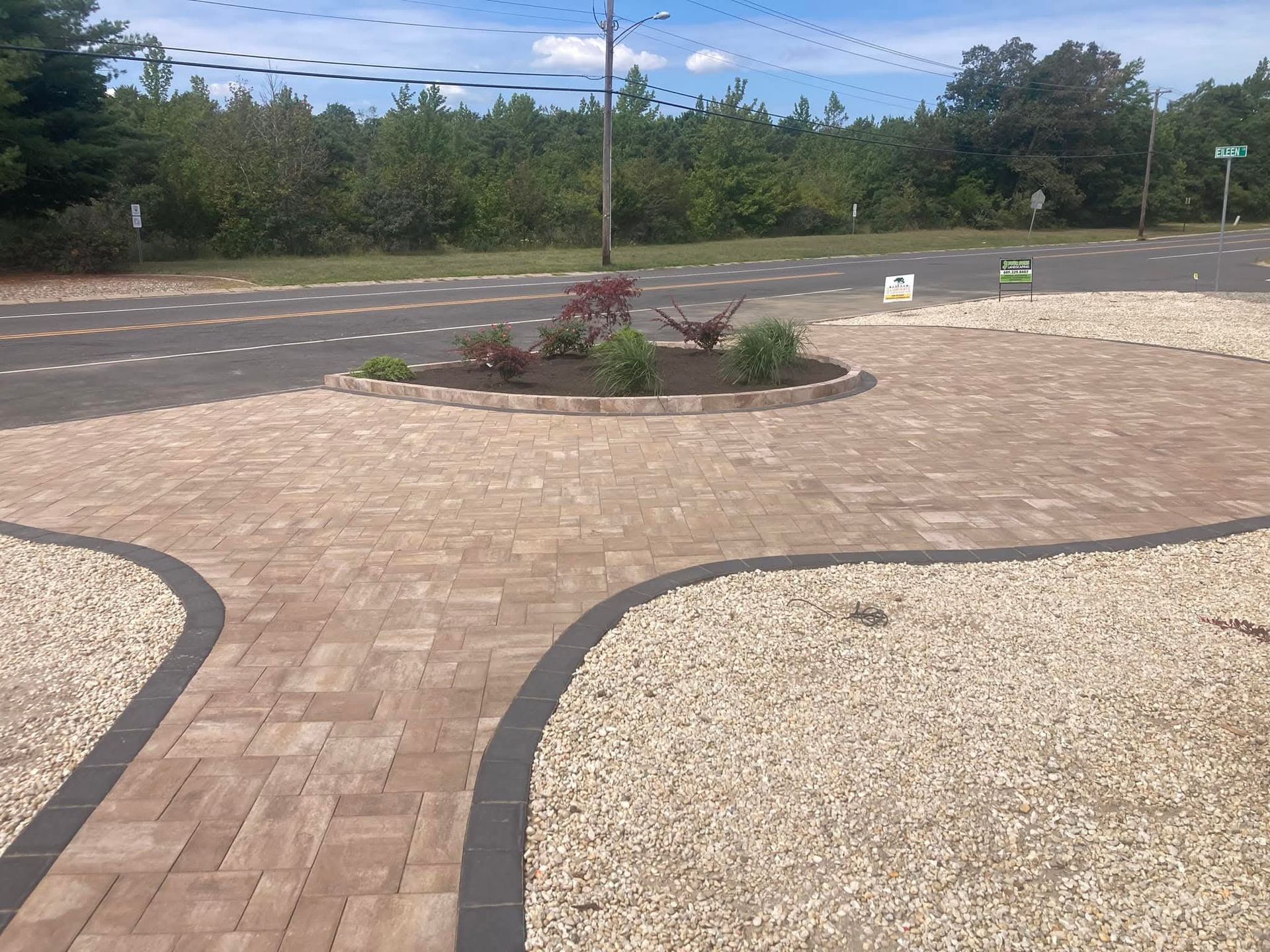 Brick paved circular driveway with a central flowerbed, bordered by gravel and a road.