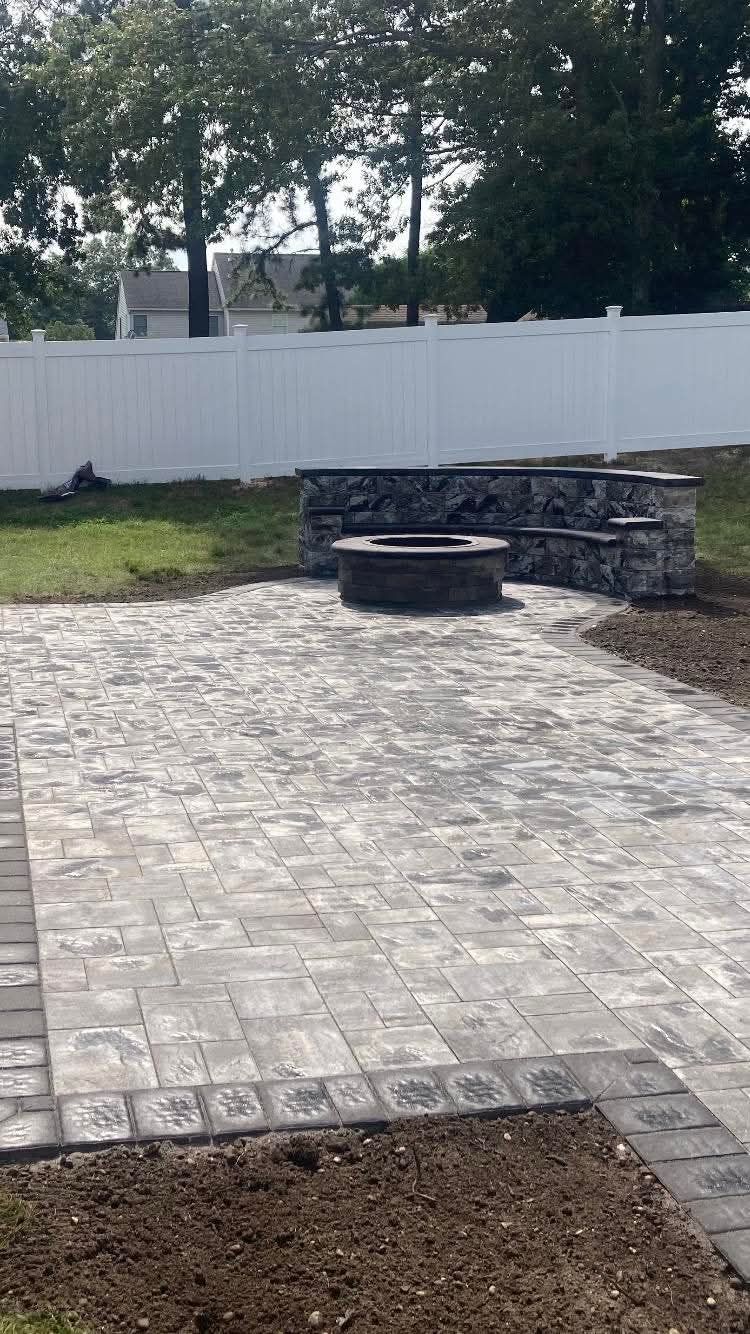 Backyard patio with fire pit, pavers, retaining wall, and white fence.