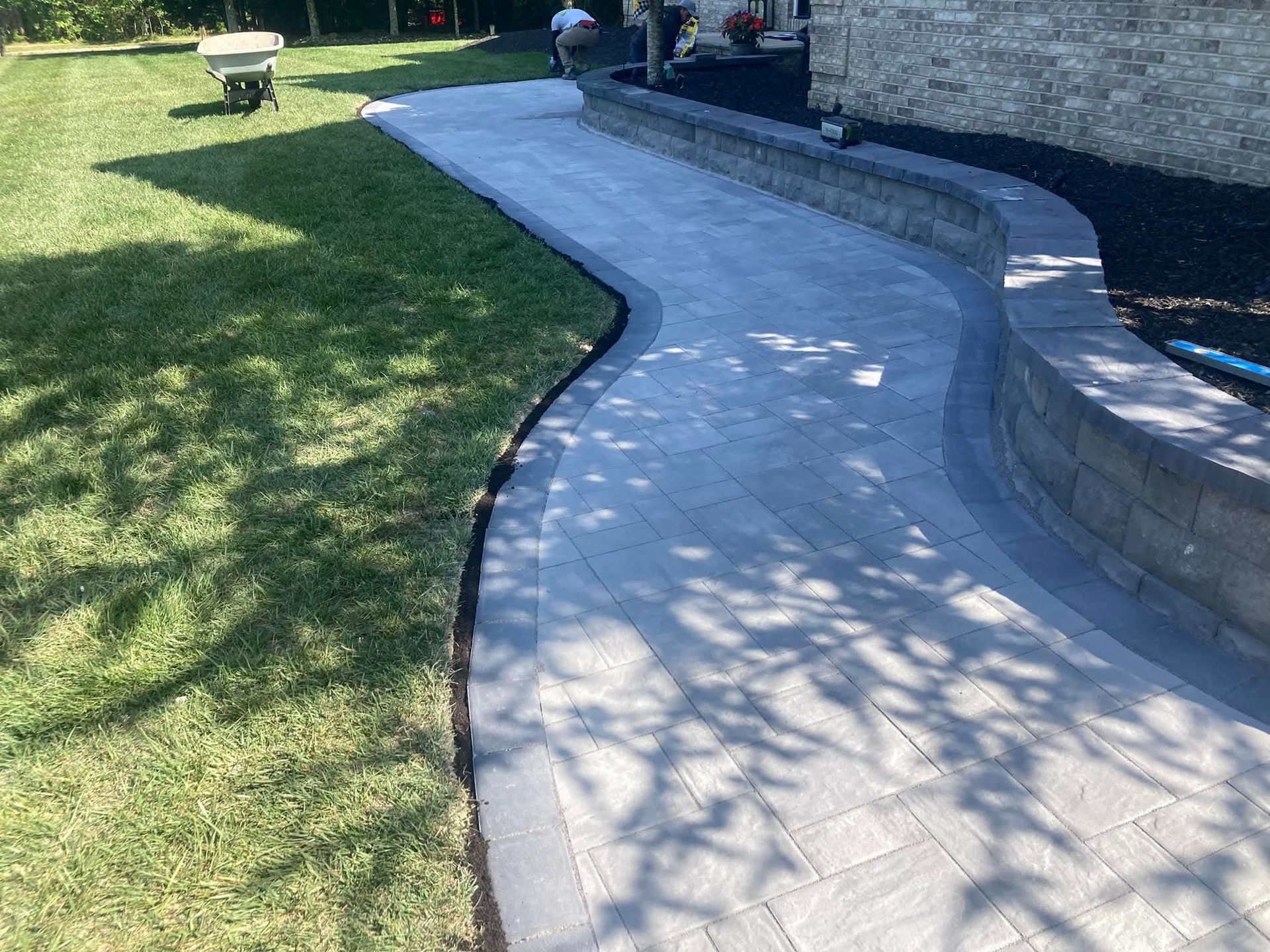 A curving paved walkway next to a low retaining wall and grass.