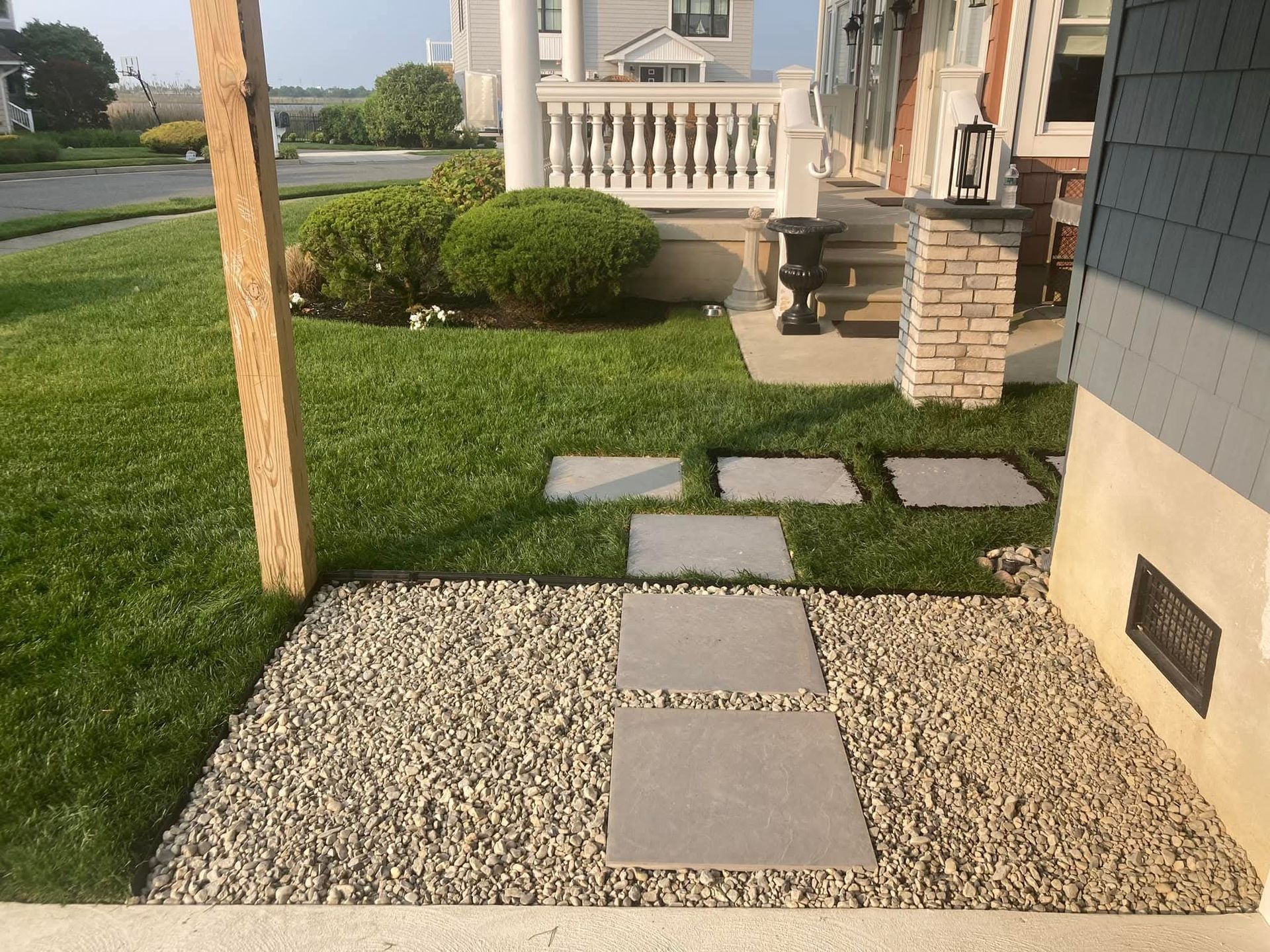 Stone pathway through gravel and grass leads to a porch with a white balustrade.