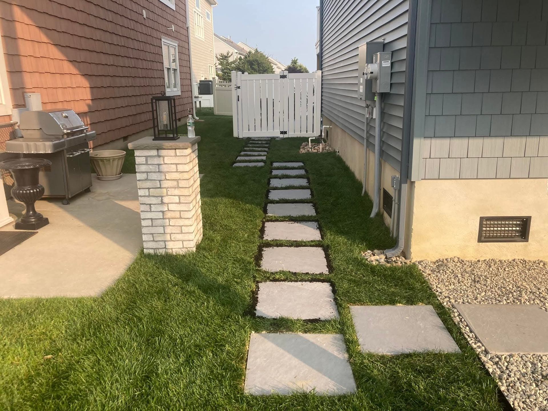 Stone path leads to white gate between two houses, flanked by green grass.