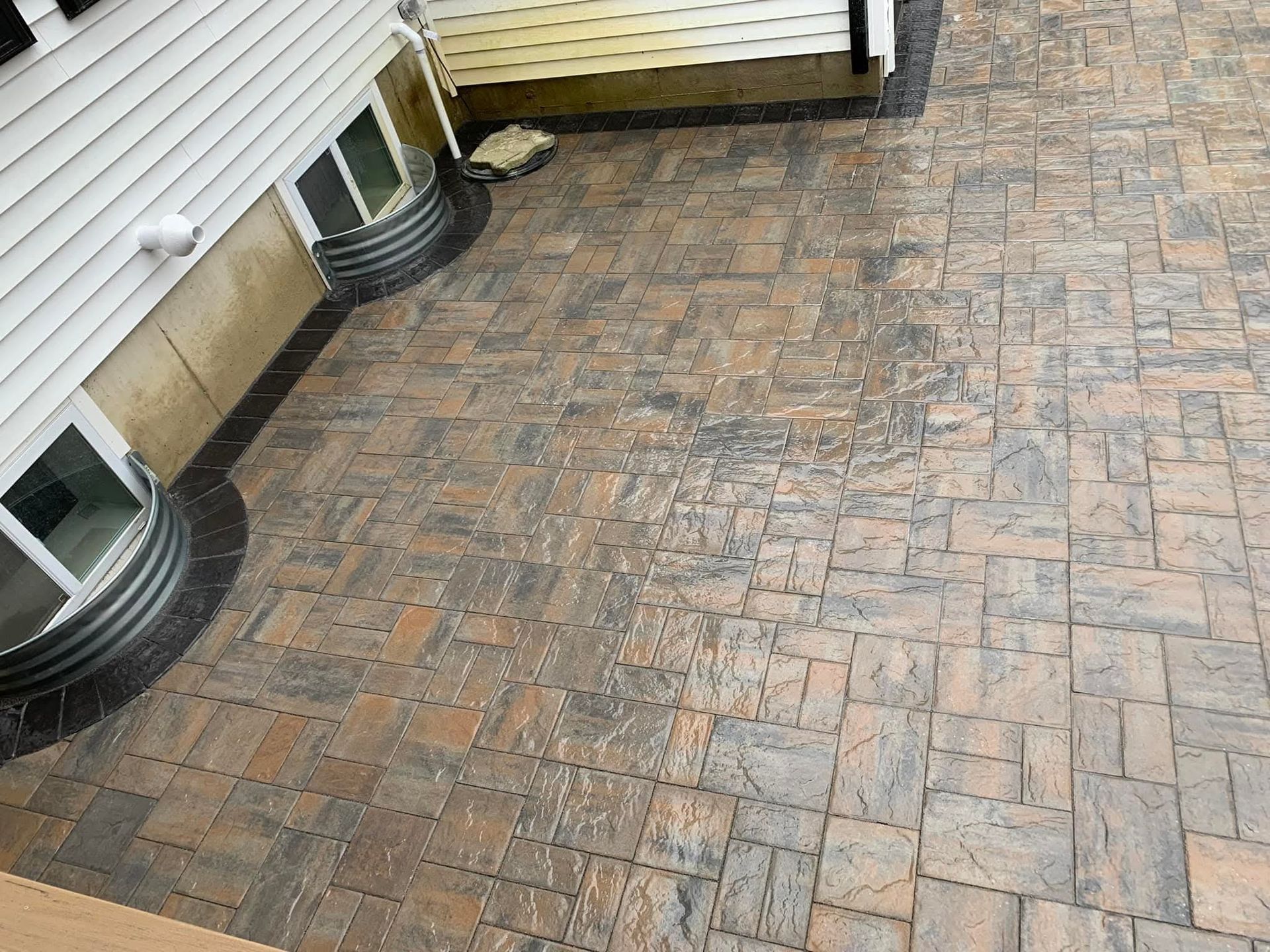 Stone paver patio outside a house with window wells.