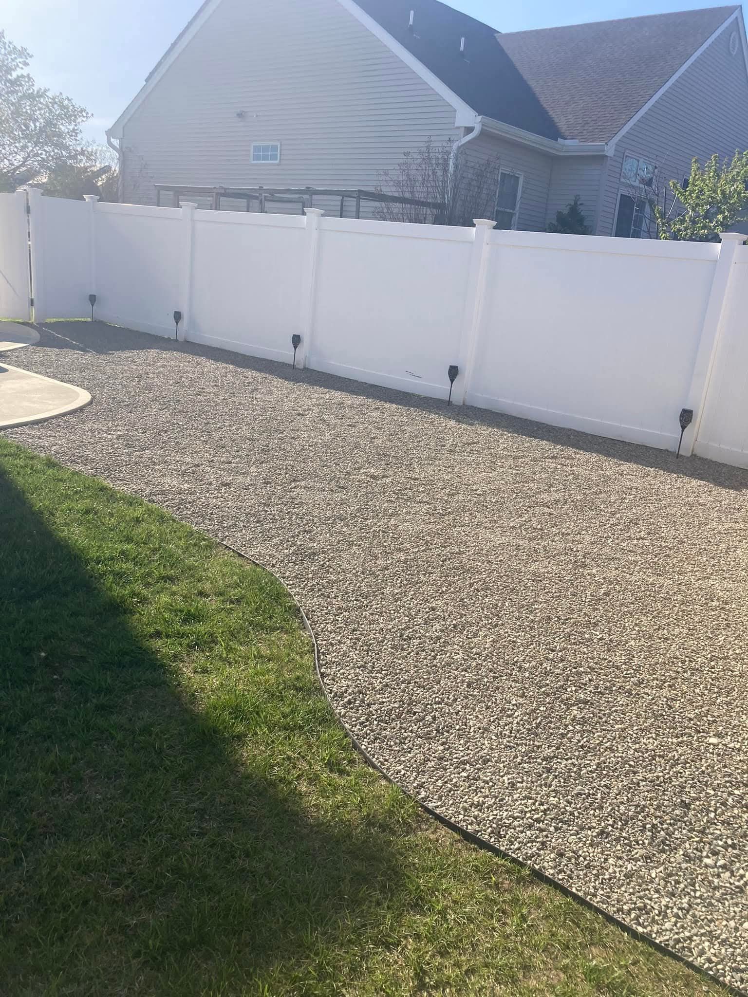 A white fence borders a gravel path next to a green lawn and a house.