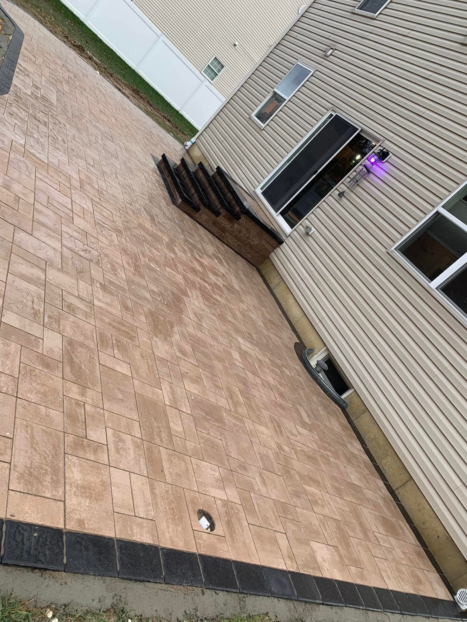 Overhead view of a house with tan siding, brown brick patio, and some dark debris.