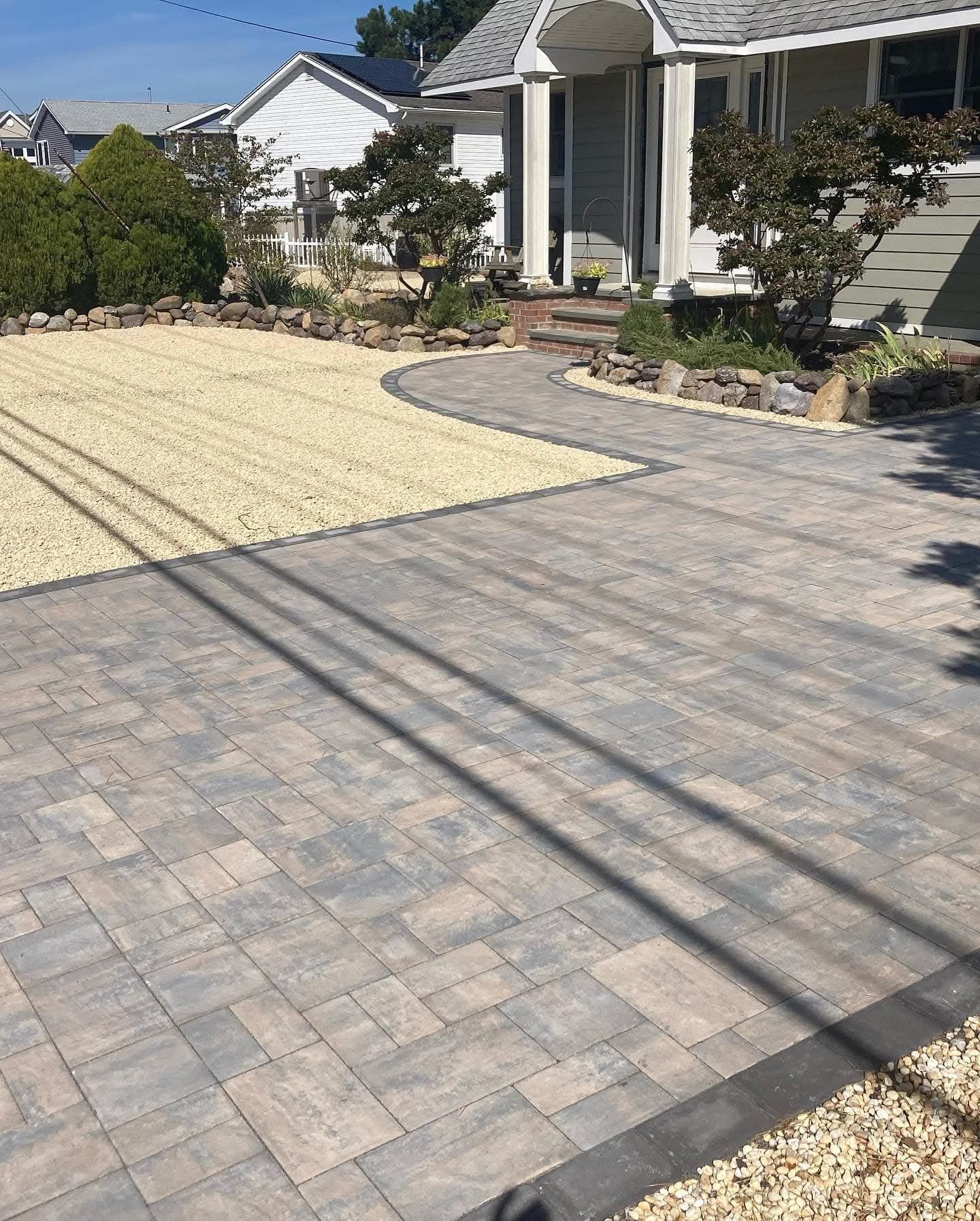 Paver driveway with gravel parking area, leading to a house.