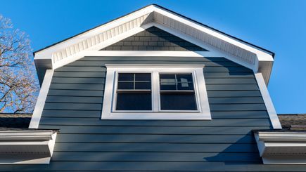 The roof of a house with a window and a blue sky in the background.