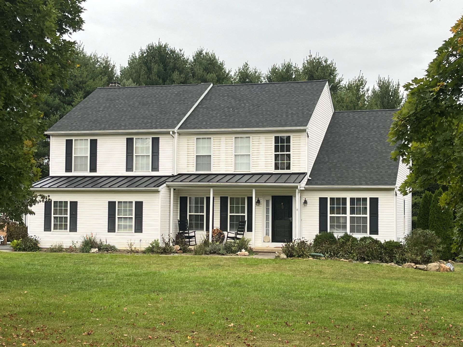 A large white house with black shutters is sitting on top of a lush green field.