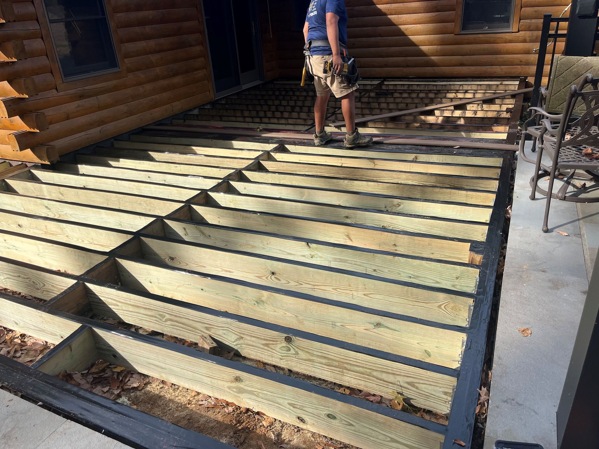 A man is standing on a wooden deck in front of a log cabin.