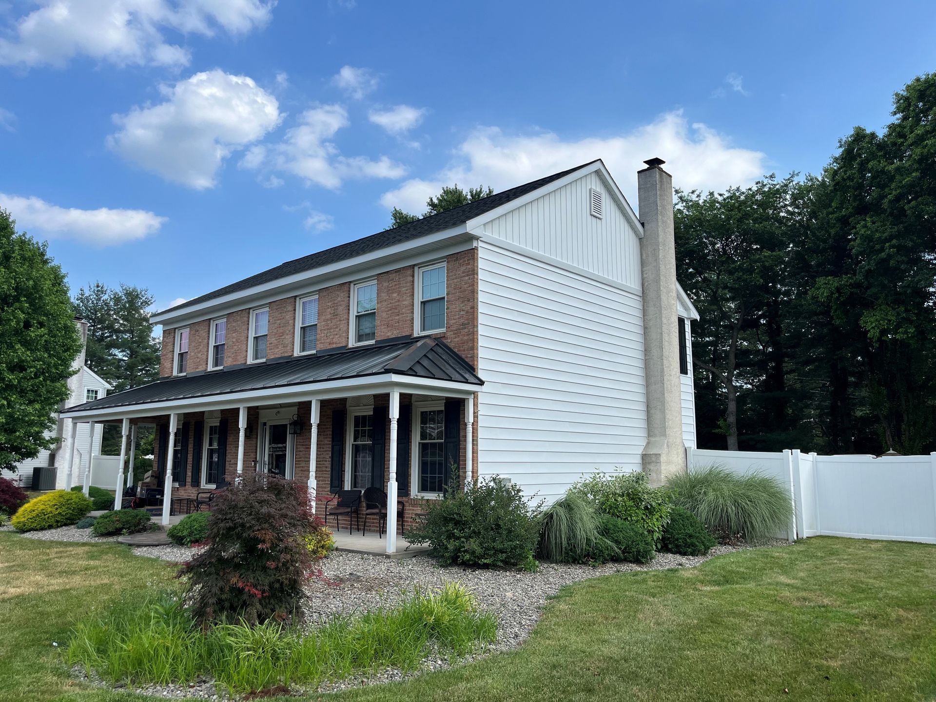 A house with a porch and a white fence in front of it.