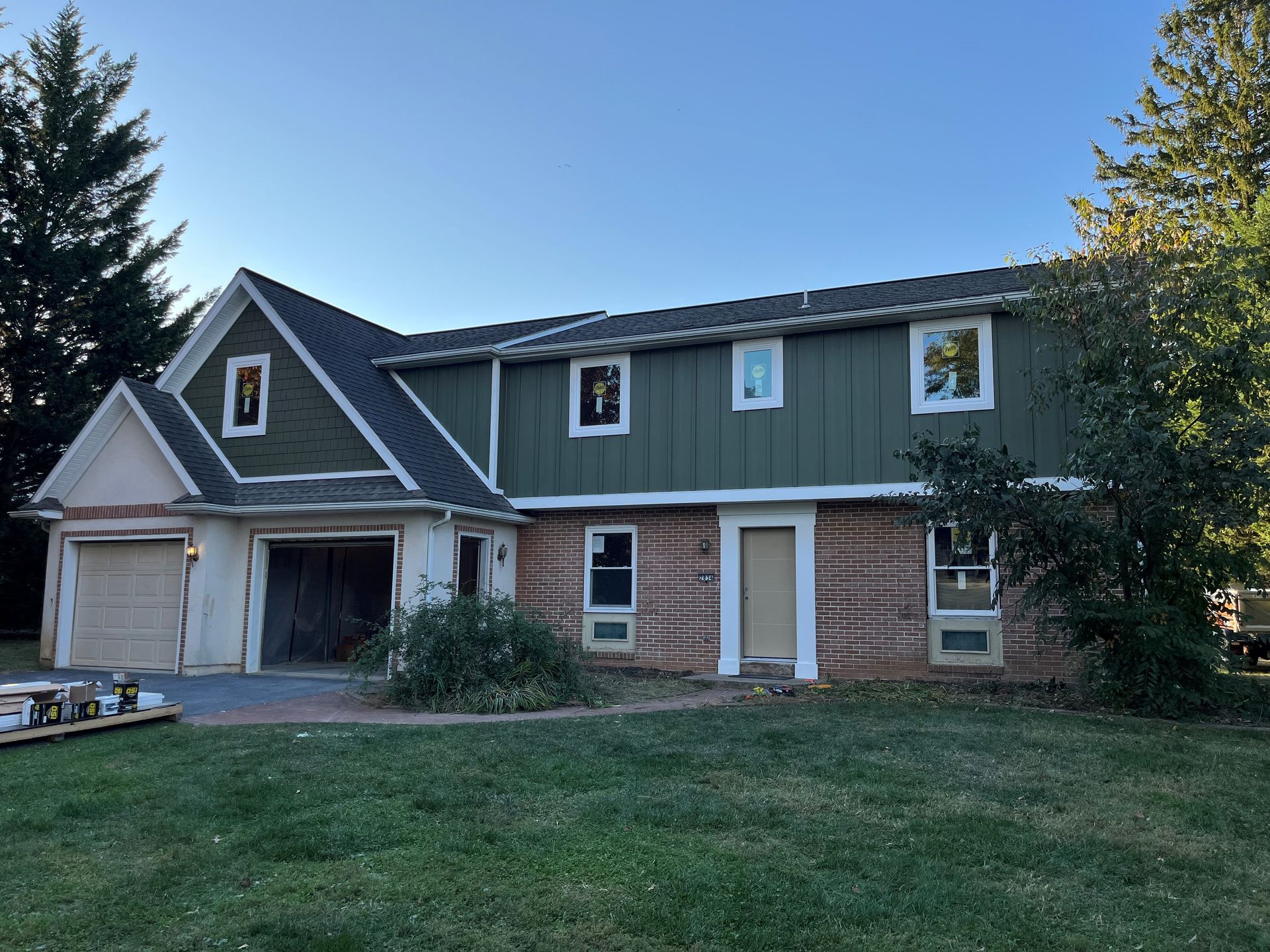 A large house with a green siding and a black roof is sitting on top of a lush green field.