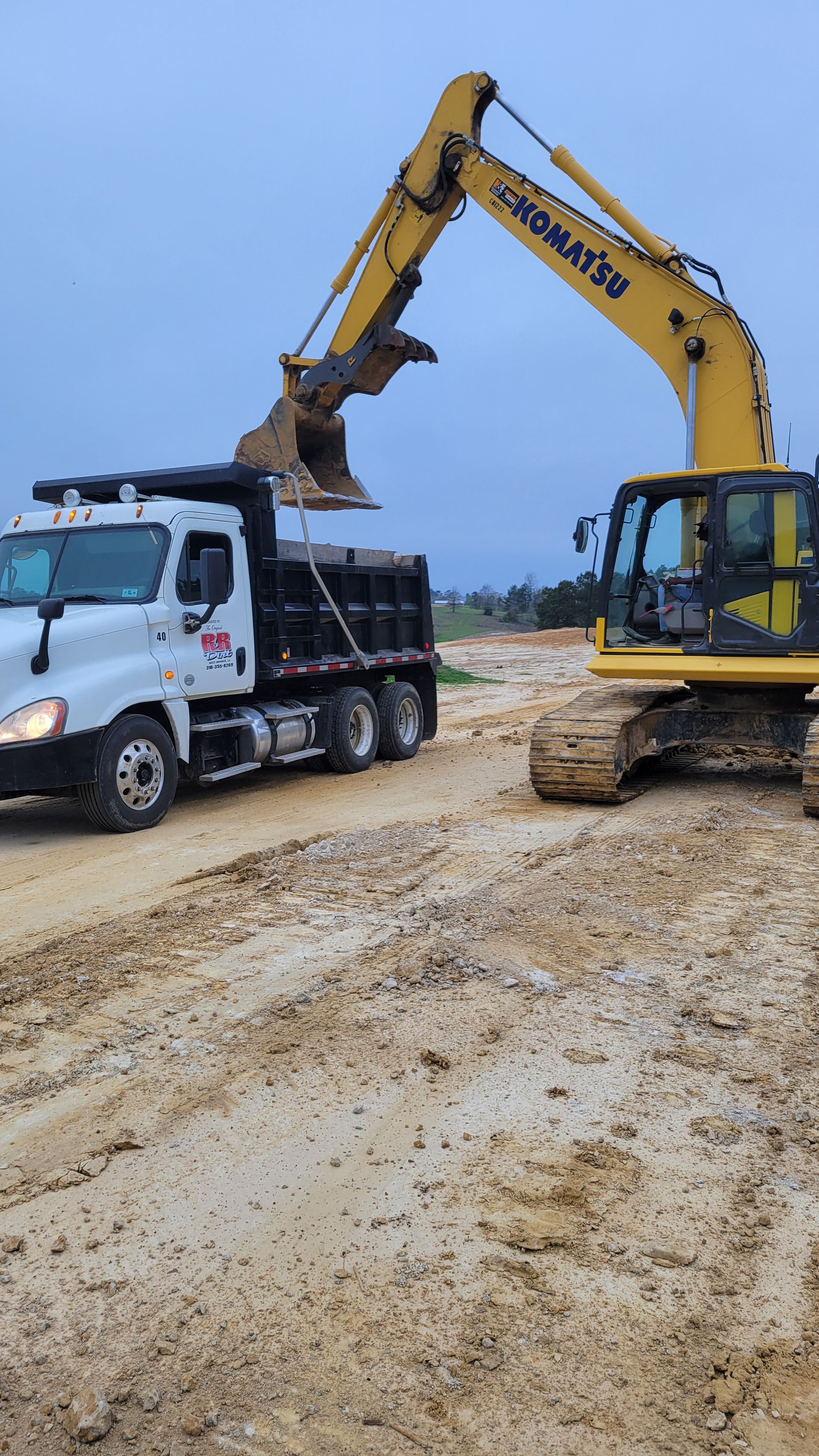 A yellow excavator loads a white dump truck.