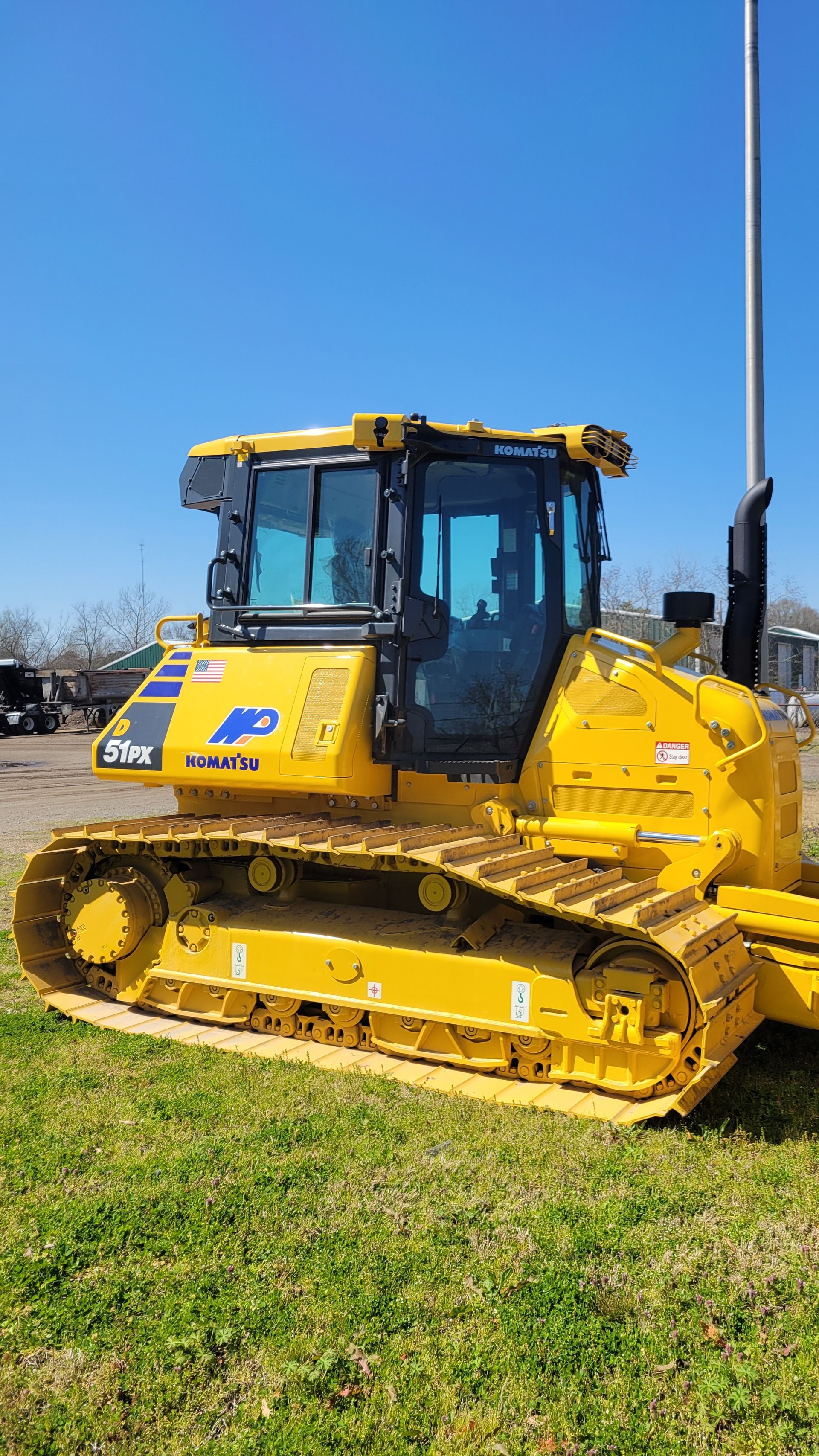 Yellow bulldozer on grass, in front of a blue sky.