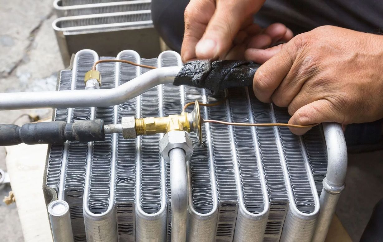 Hands working on an air conditioning condenser unit, connecting tubes and fittings with tools.
