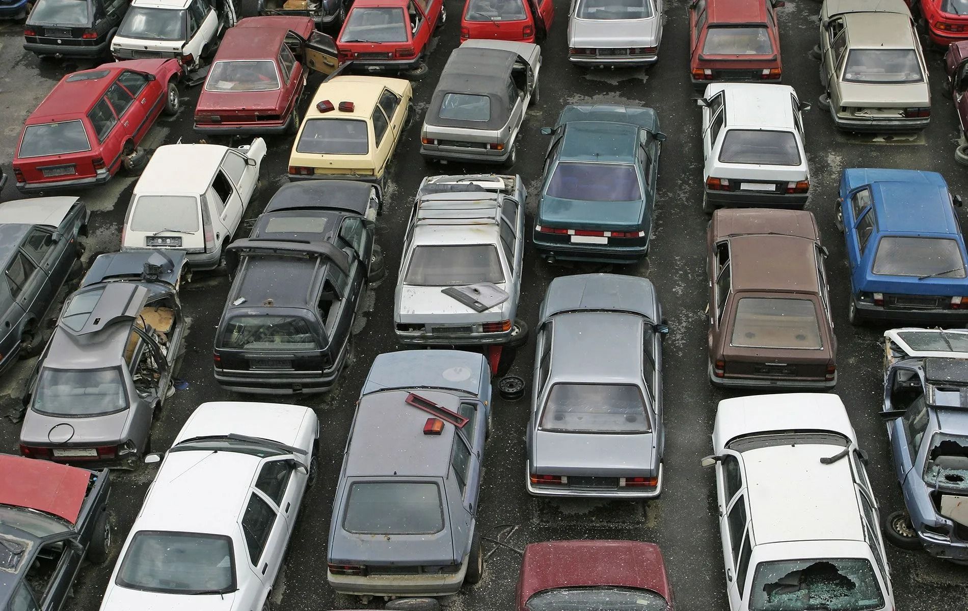 Overhead view of a junkyard filled with various cars, many in shades of red, white, and gray.