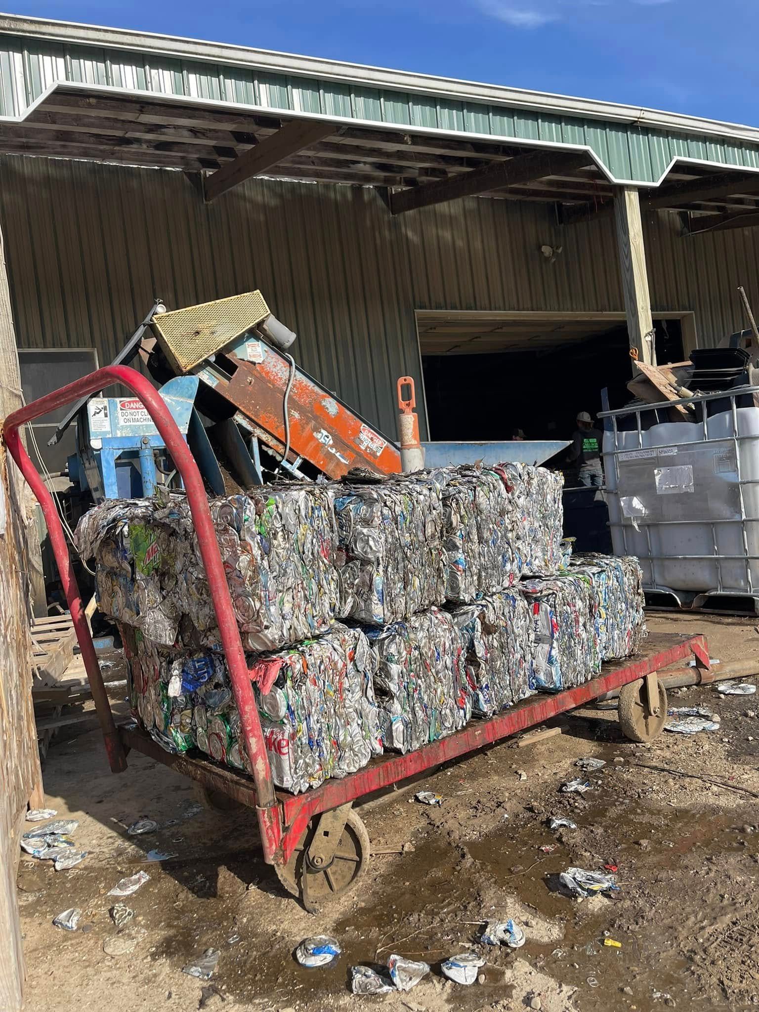 Red hand truck loaded with compressed plastic bales near a recycling facility.