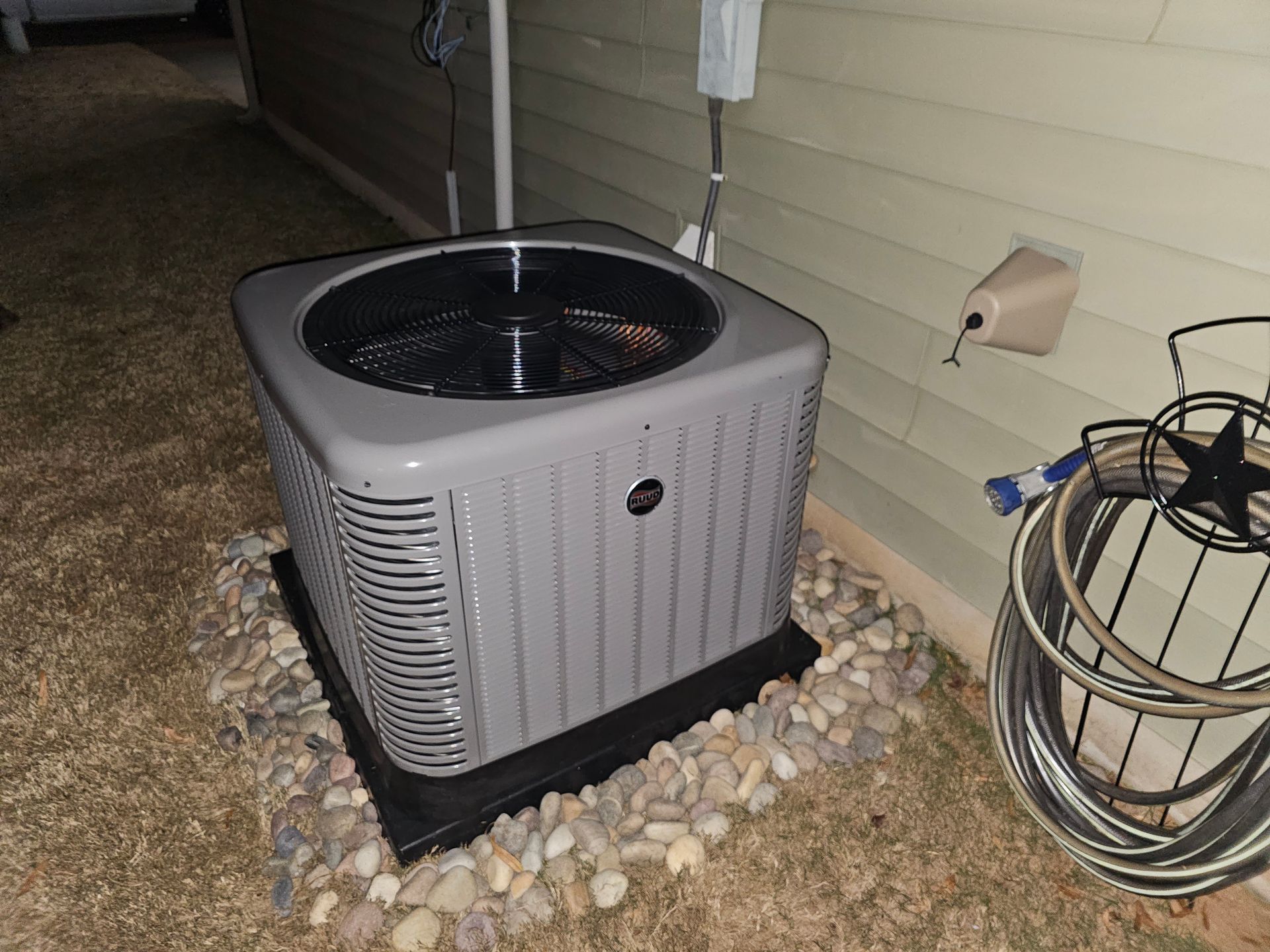 An air conditioner is sitting on the side of a house next to a hose