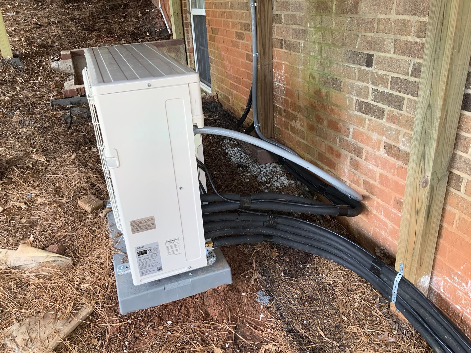 A white air conditioner is sitting next to a brick wall