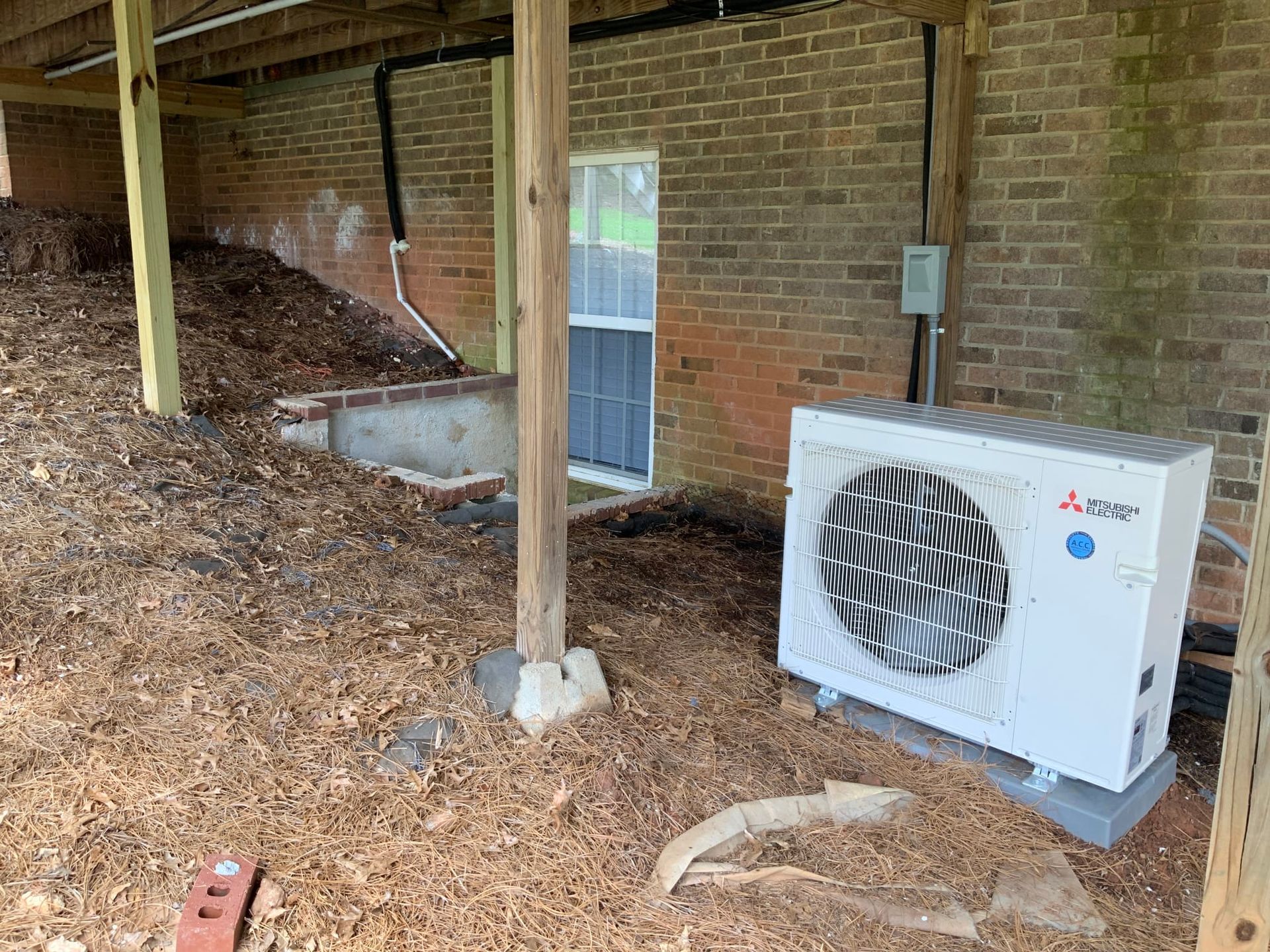 A white air conditioner is sitting next to a brick wall