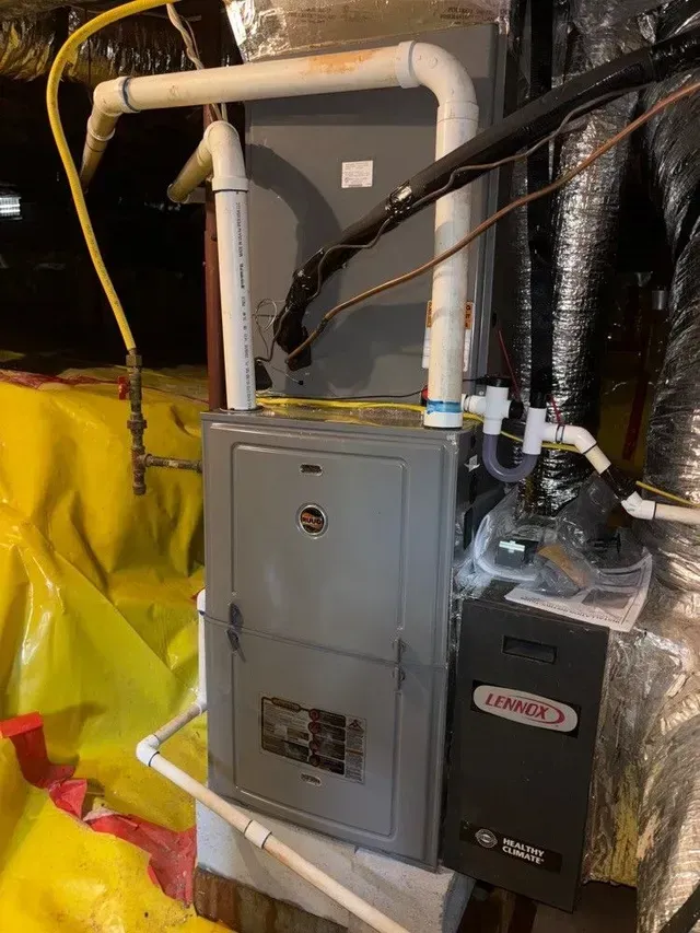 A gas furnace is sitting in a basement next to a yellow tarp