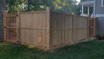 A wooden picket fence is surrounded by trees and bushes in front of a house