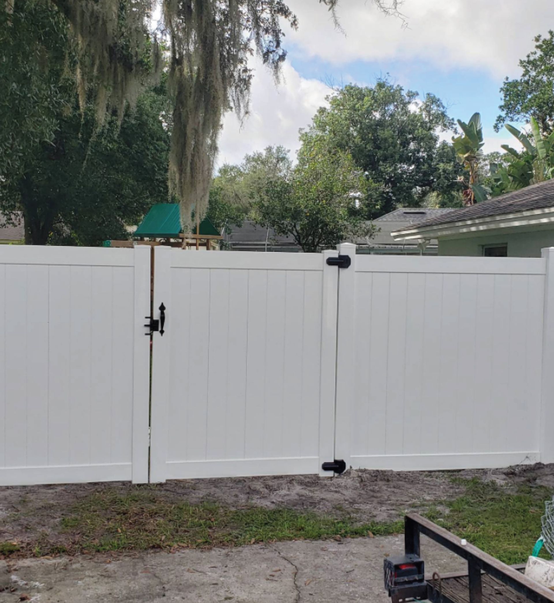 White wooden fence with a central gate in a backyard, with trees and rooftops visible above it