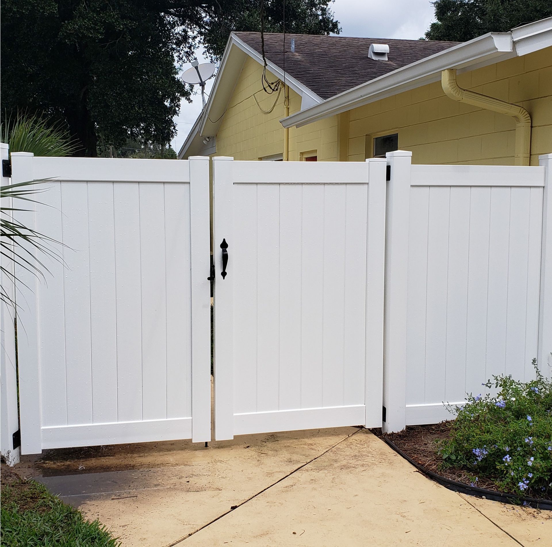 White wooden fence gate blocking a driveway beside a yellow house and walkway