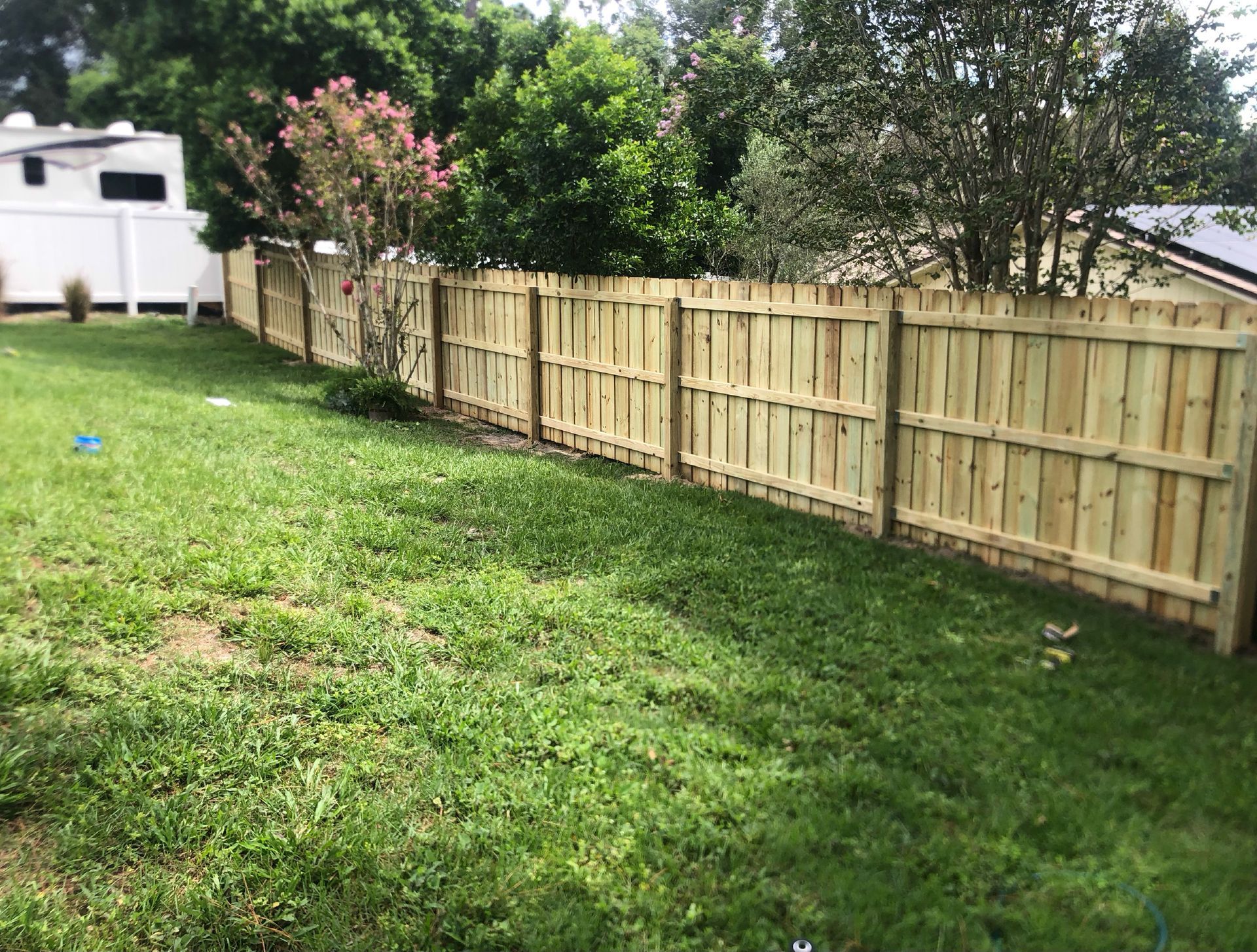 Grassy backyard with a wooden fence, white shed, and trees in the background.