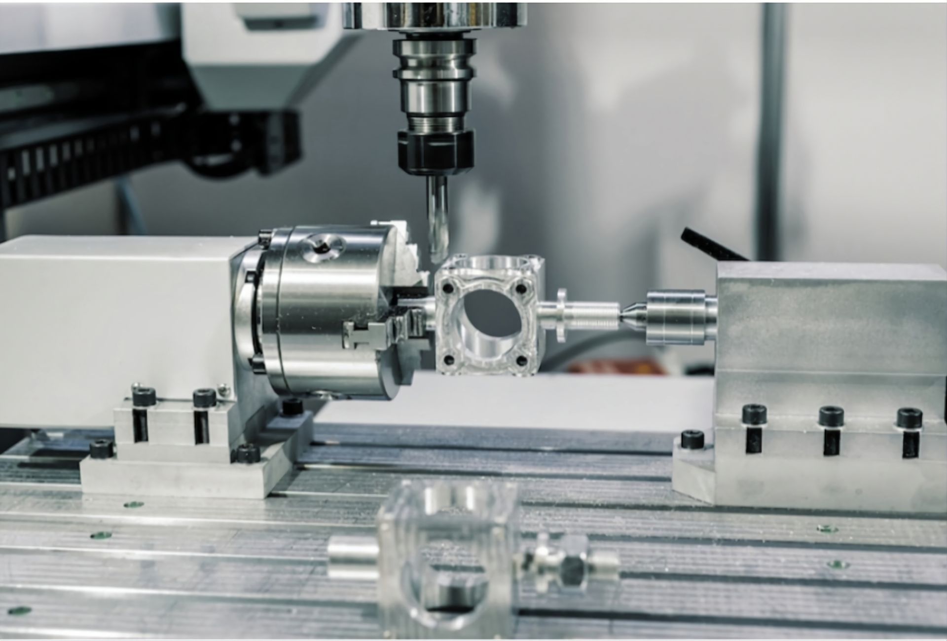 A CNC milling machine machining a metal component held between a rotary chuck and a tailstock on a workshop table.