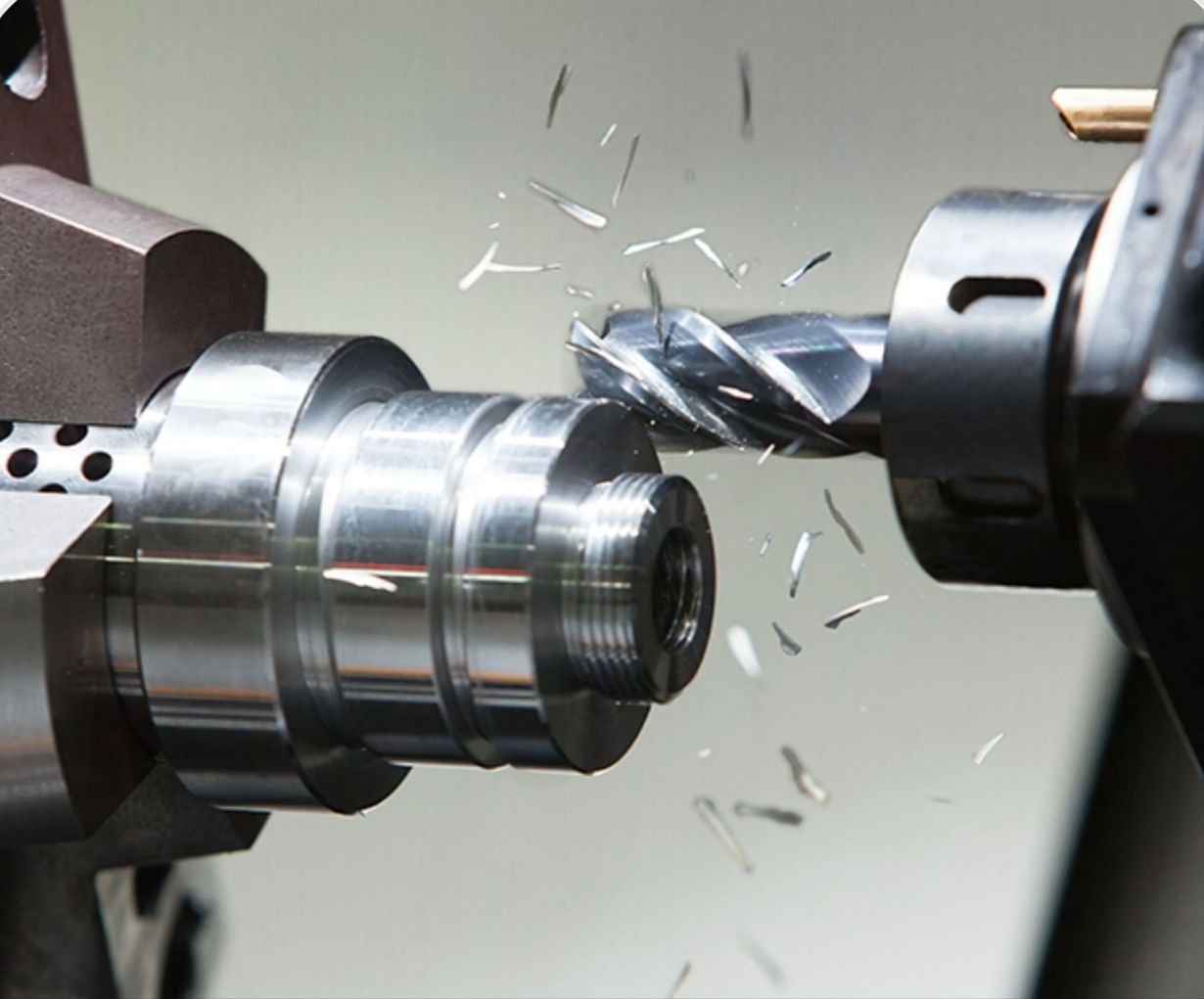 A metal milling cutter machining a steel cylindrical part, creating metal shavings in an industrial workshop.