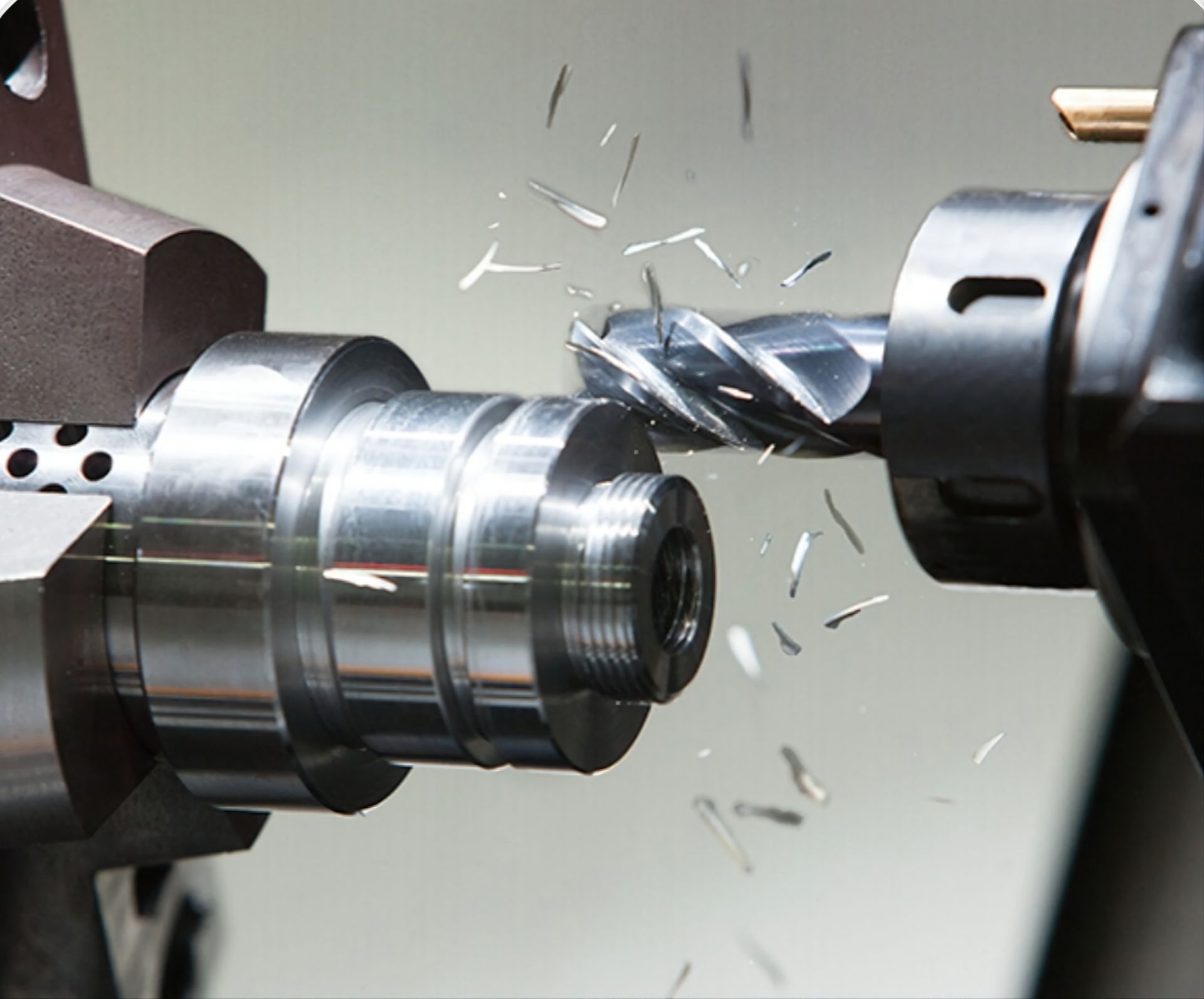 A metal milling cutter machining a steel cylindrical part, creating metal shavings in an industrial workshop.
