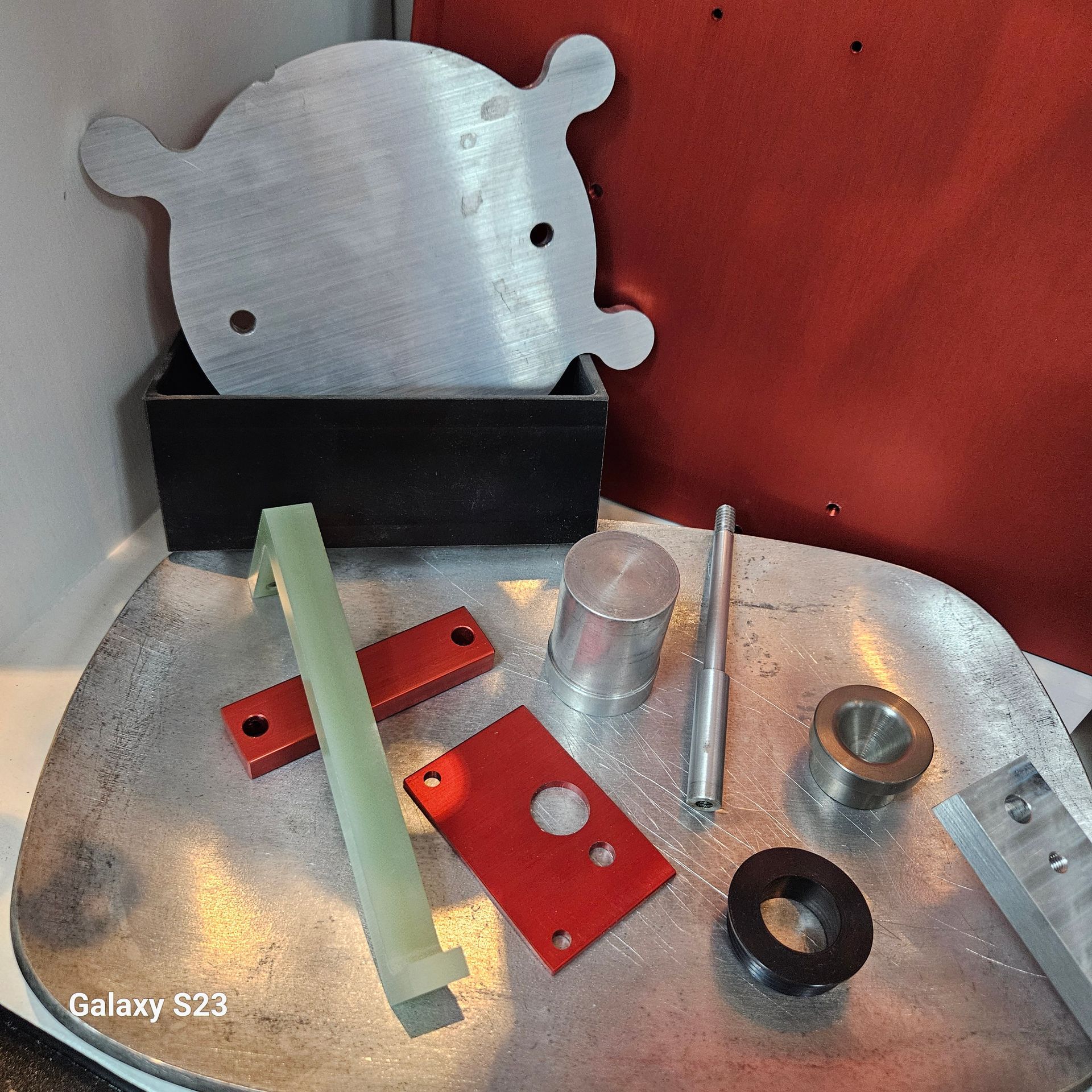 Various metal and composite industrial components, including plates, bars, and cylindrical parts, rest on a metal surface.