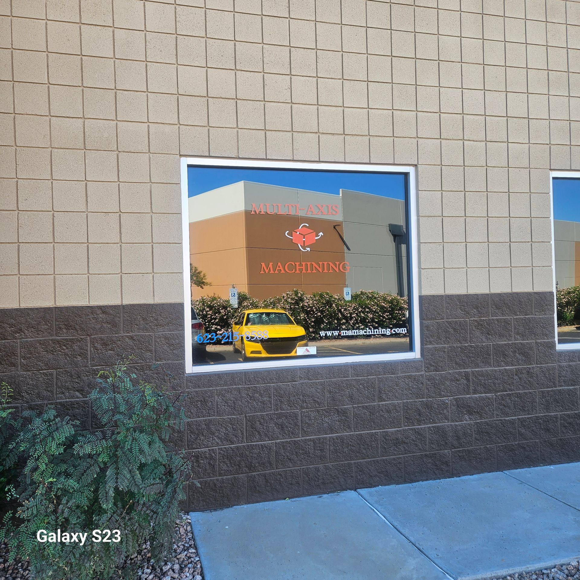 A window on a tan brick building reflecting a yellow car and a business logo reading 