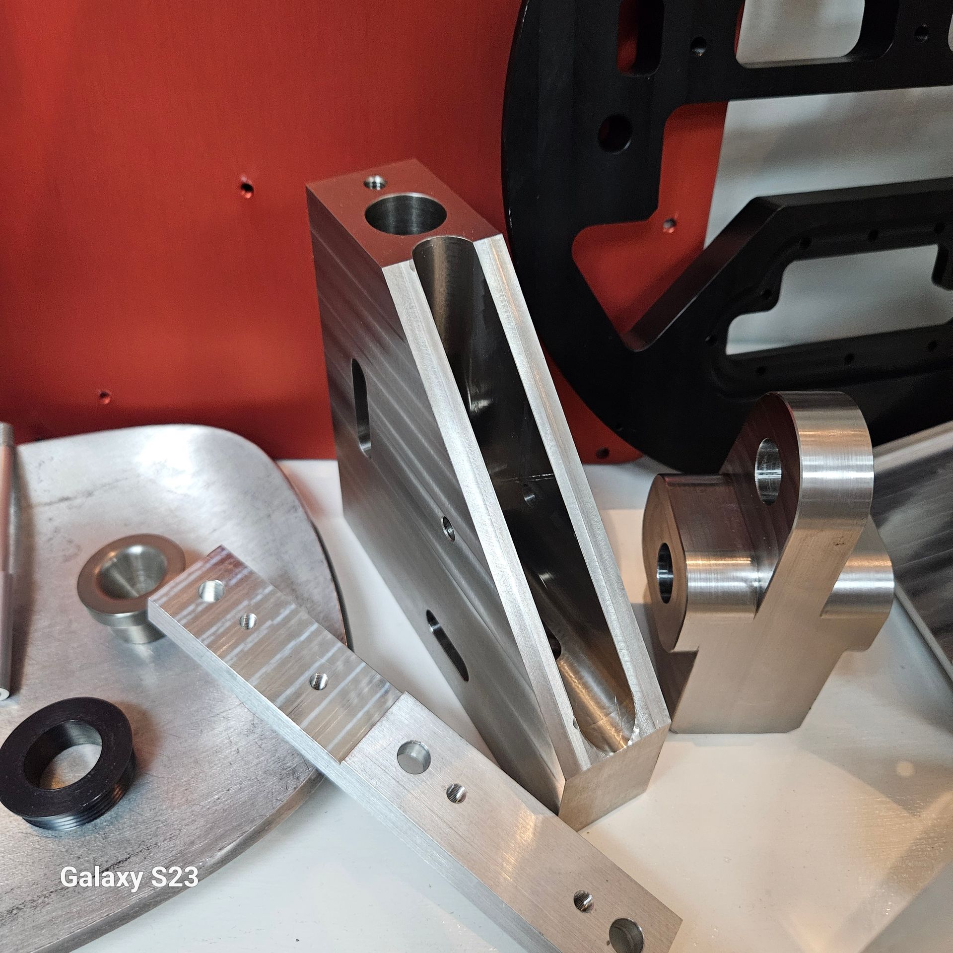 A collection of various precision-machined metal components and a black bracket resting on a workbench.