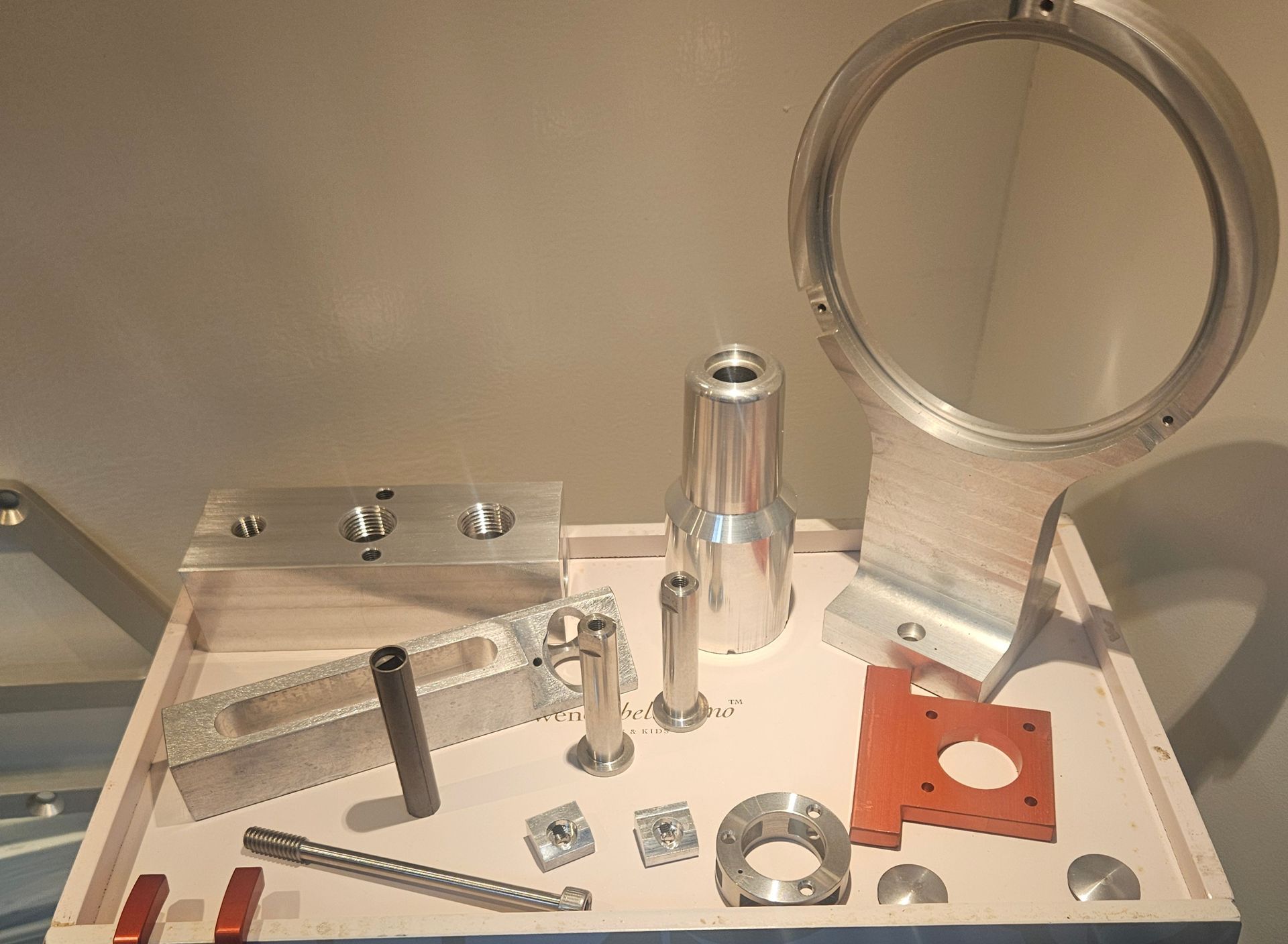 An assortment of machined metal mechanical parts and a red component arranged on a light-colored workbench.