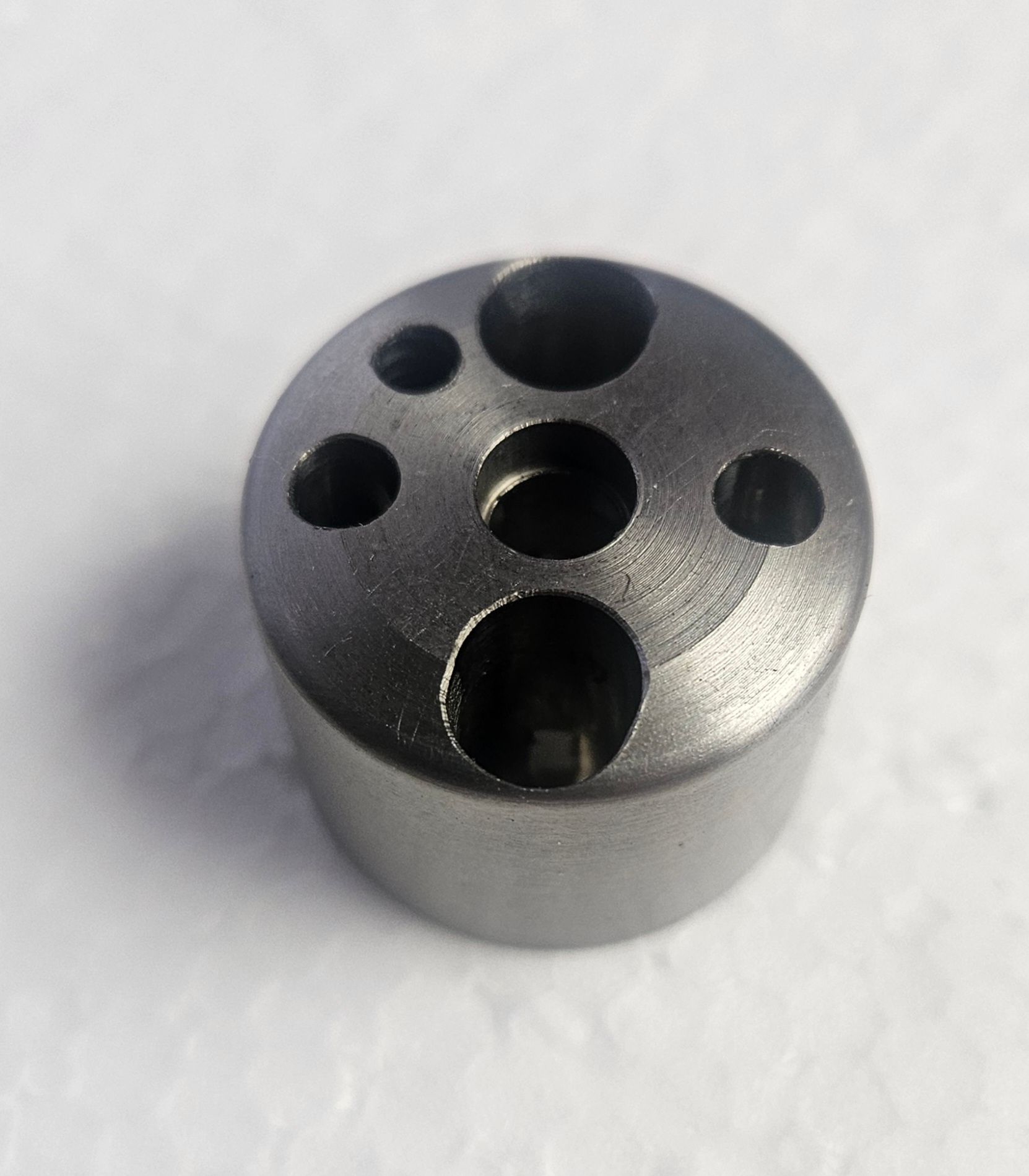 A small, cylindrical metal component with a central hole surrounded by four varying-sized holes on its top surface.