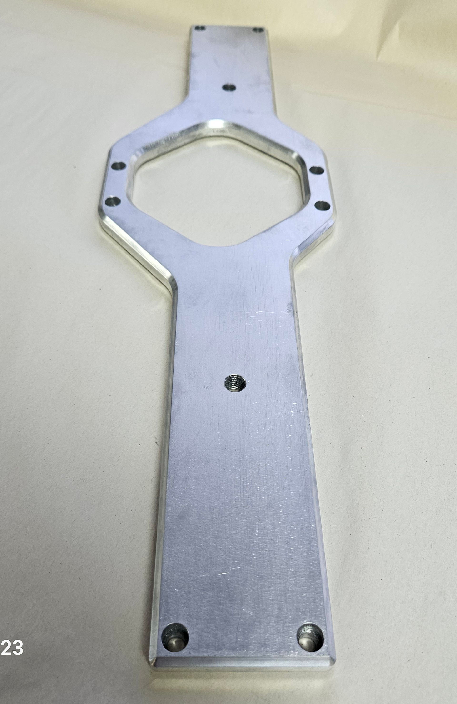 A flat, silver, metallic mounting plate with a central hexagonal opening and several pre-drilled circular bolt holes.
