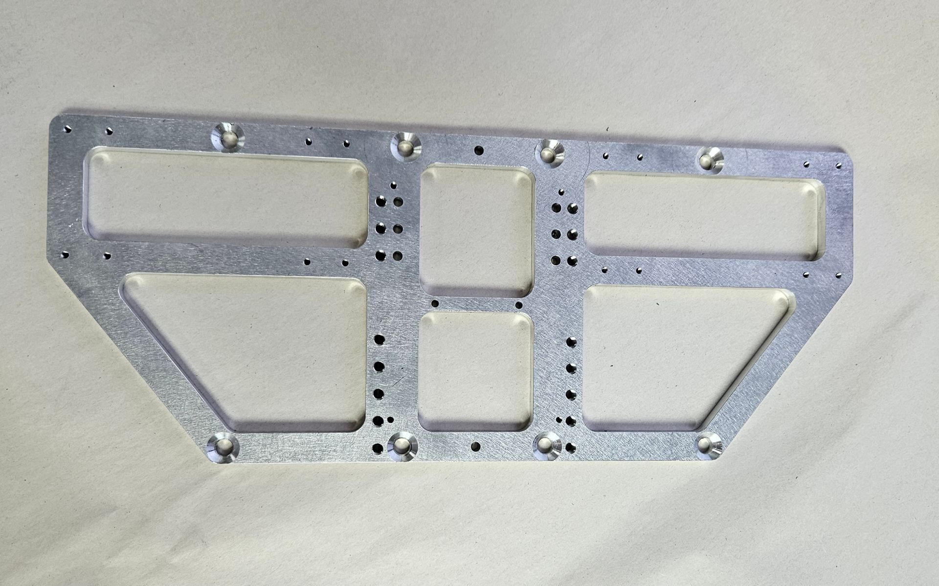 A rectangular, silver-colored metal plate with cut-out sections and multiple evenly spaced pre-drilled holes.