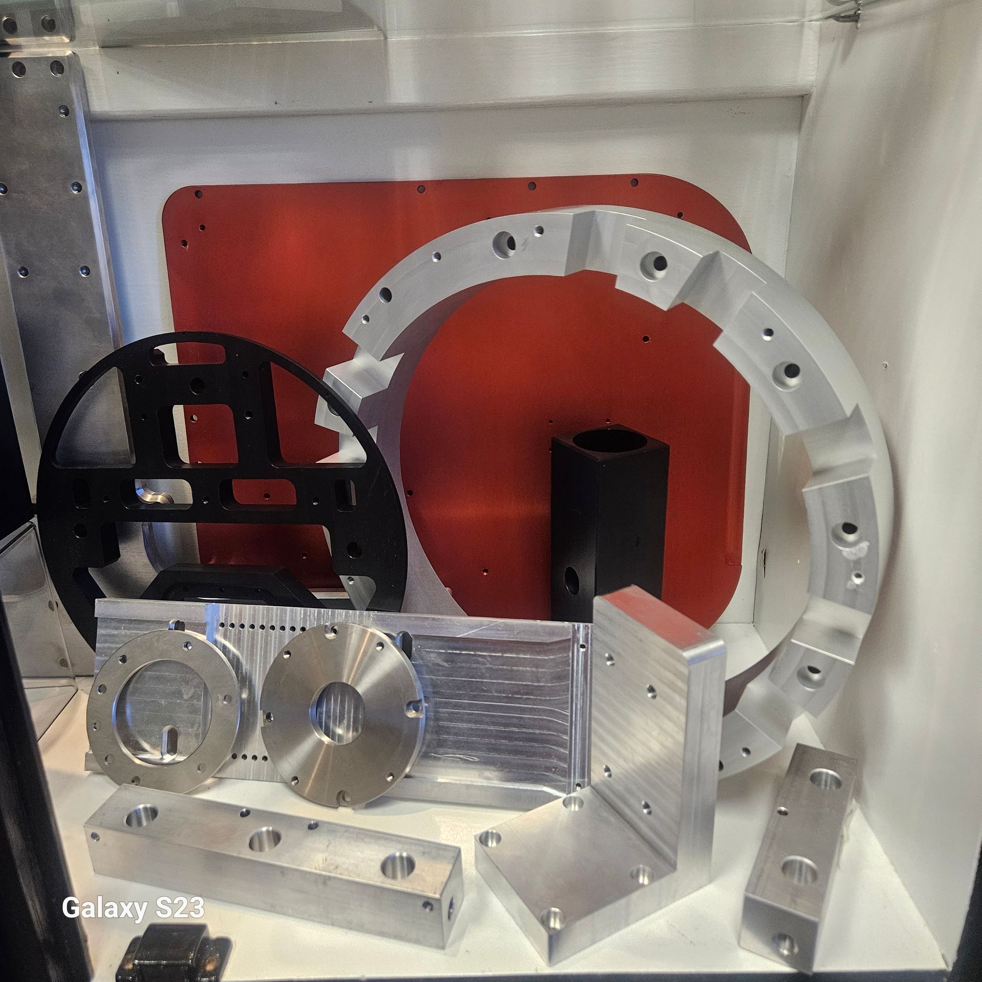 A collection of precision-machined metal industrial parts, including rings, blocks, and plates, displayed on a shelf.