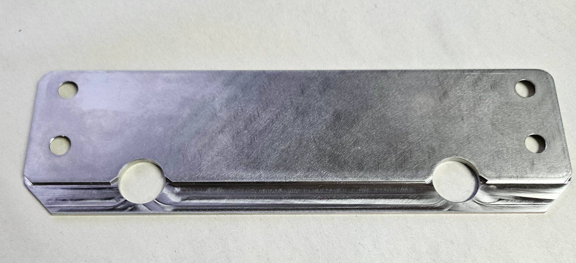 A rectangular, metallic mounting bracket with four corner holes and two centered circular cutouts along the bottom edge.